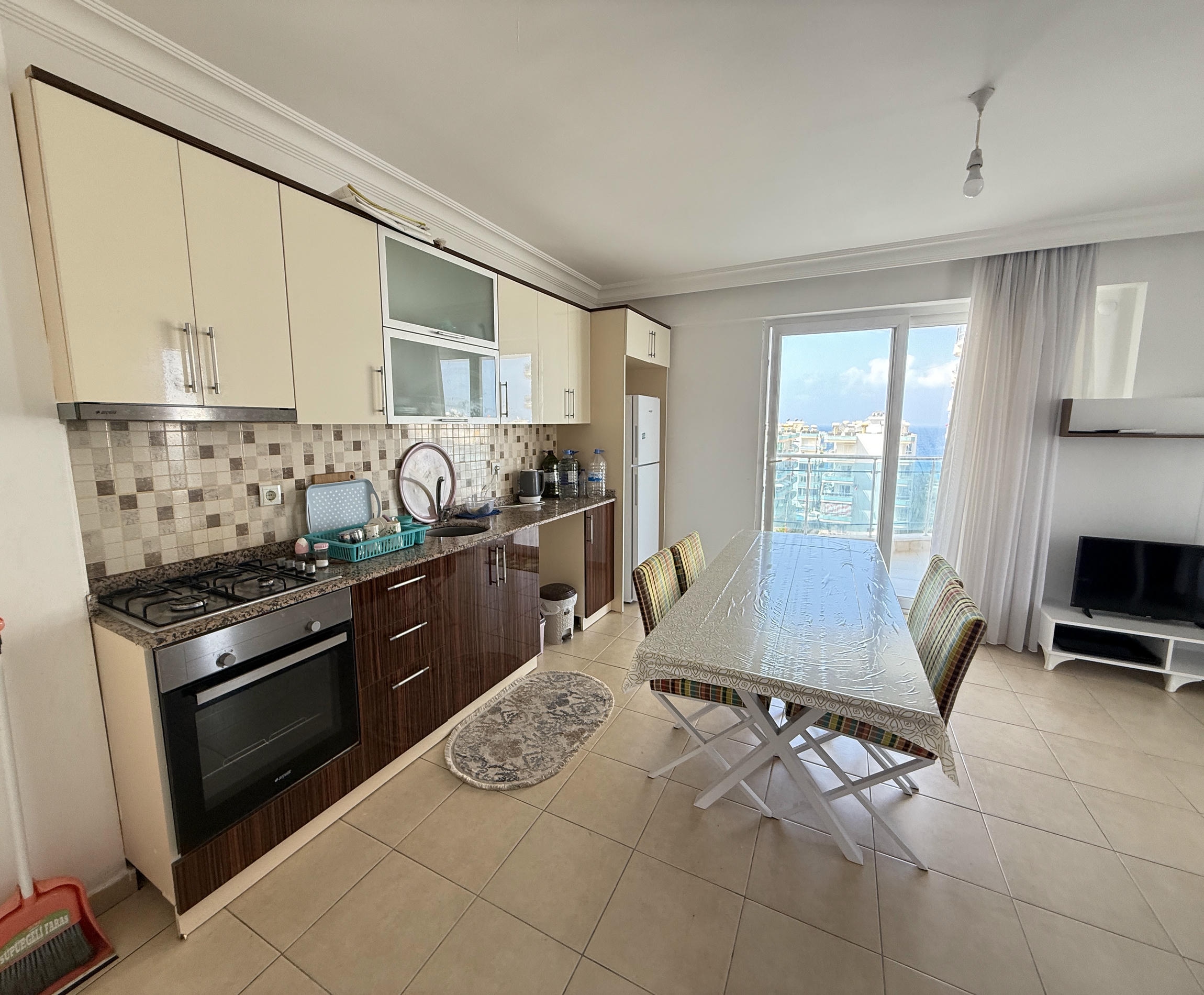 Mozaik backsplashli mutfak-salon Mahmutlar’daki dairede deniz manzaralı panoramik pencereye açılıyor