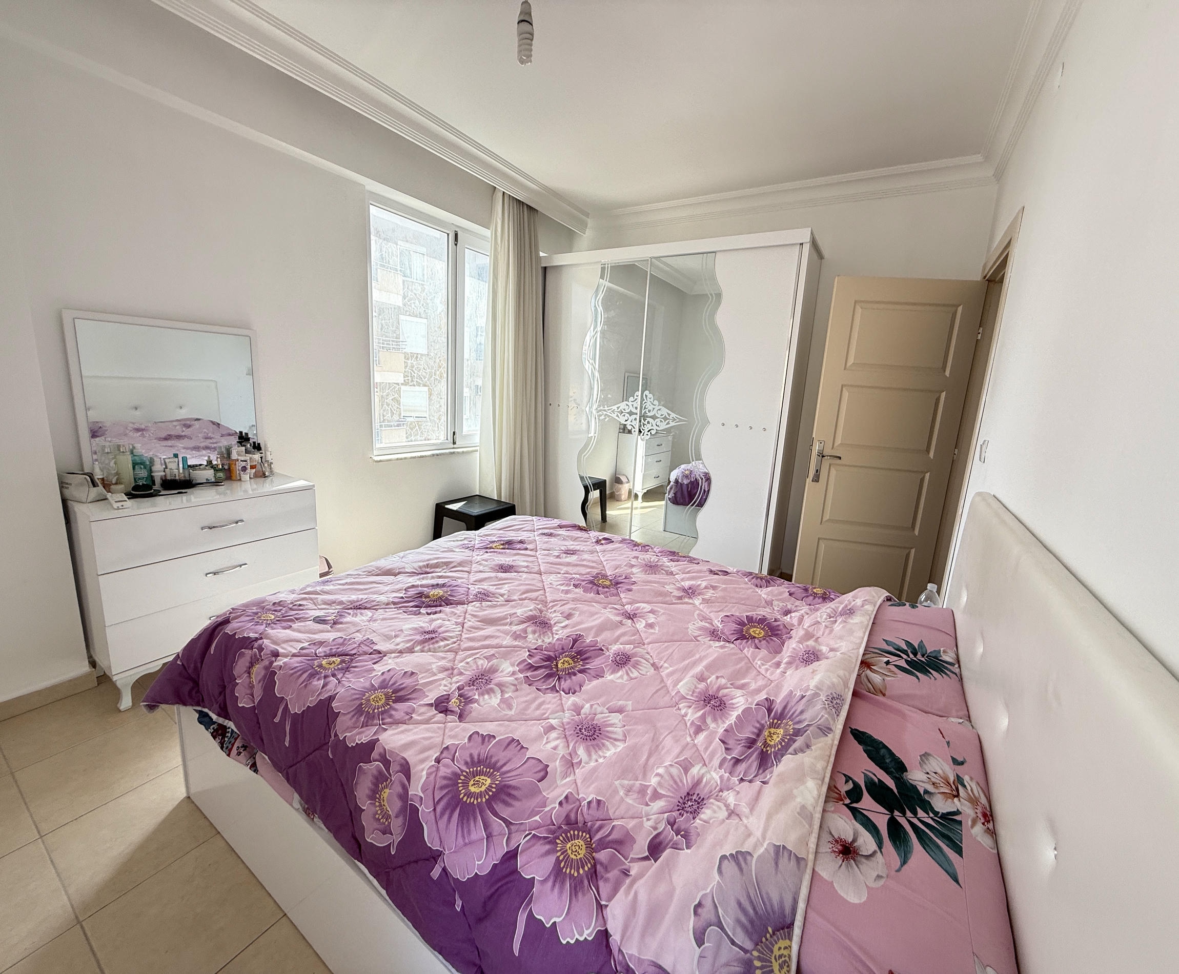Renkli örtülü yatak odası, aynalı gardırop ve panoramik penceresiyle daire içinde yer alıyor