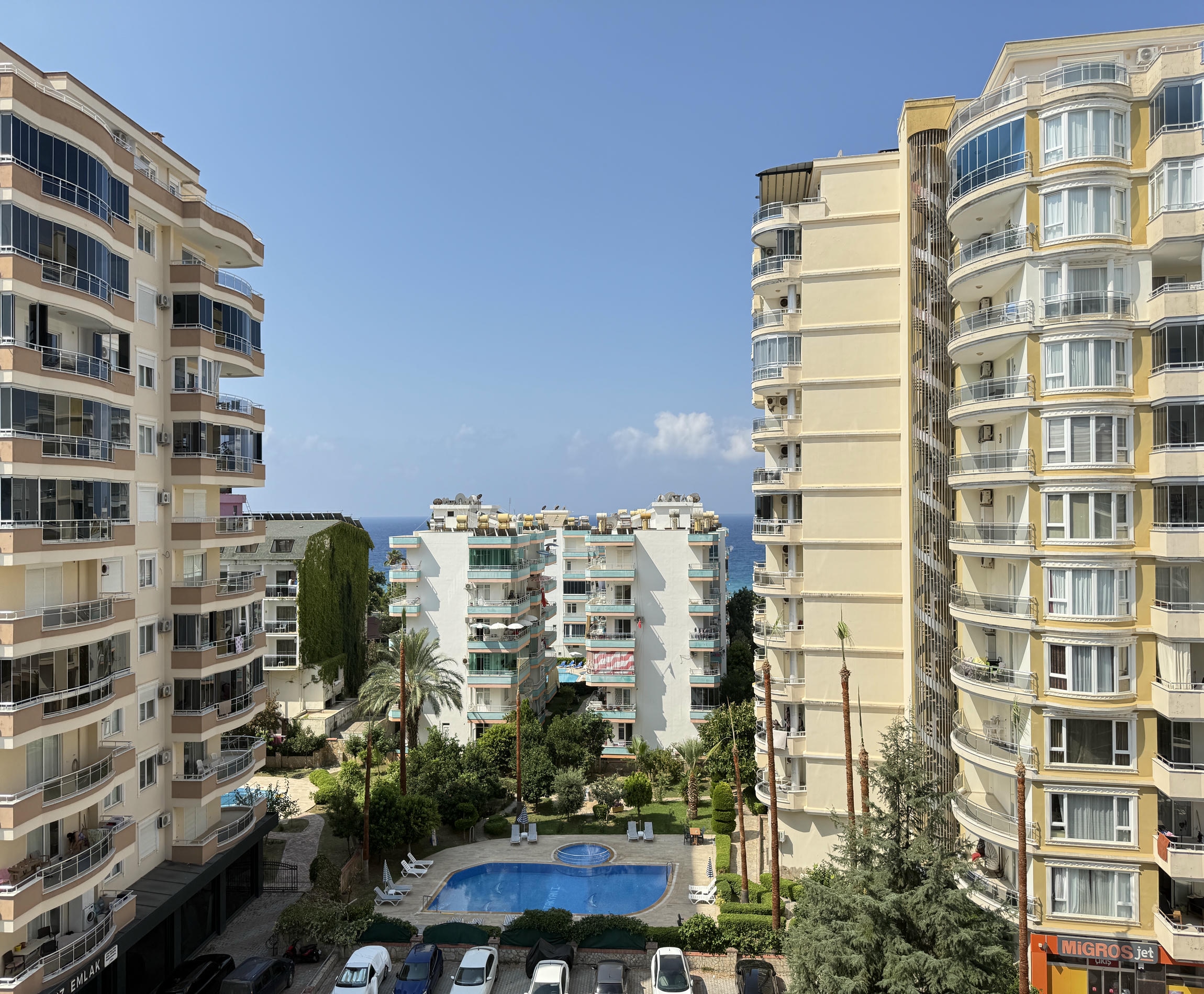 Türkiye’de dairelerin bulunduğu sitede yuvarlak açık havuz, palmiyeler ve bina cepheleri bulunuyor