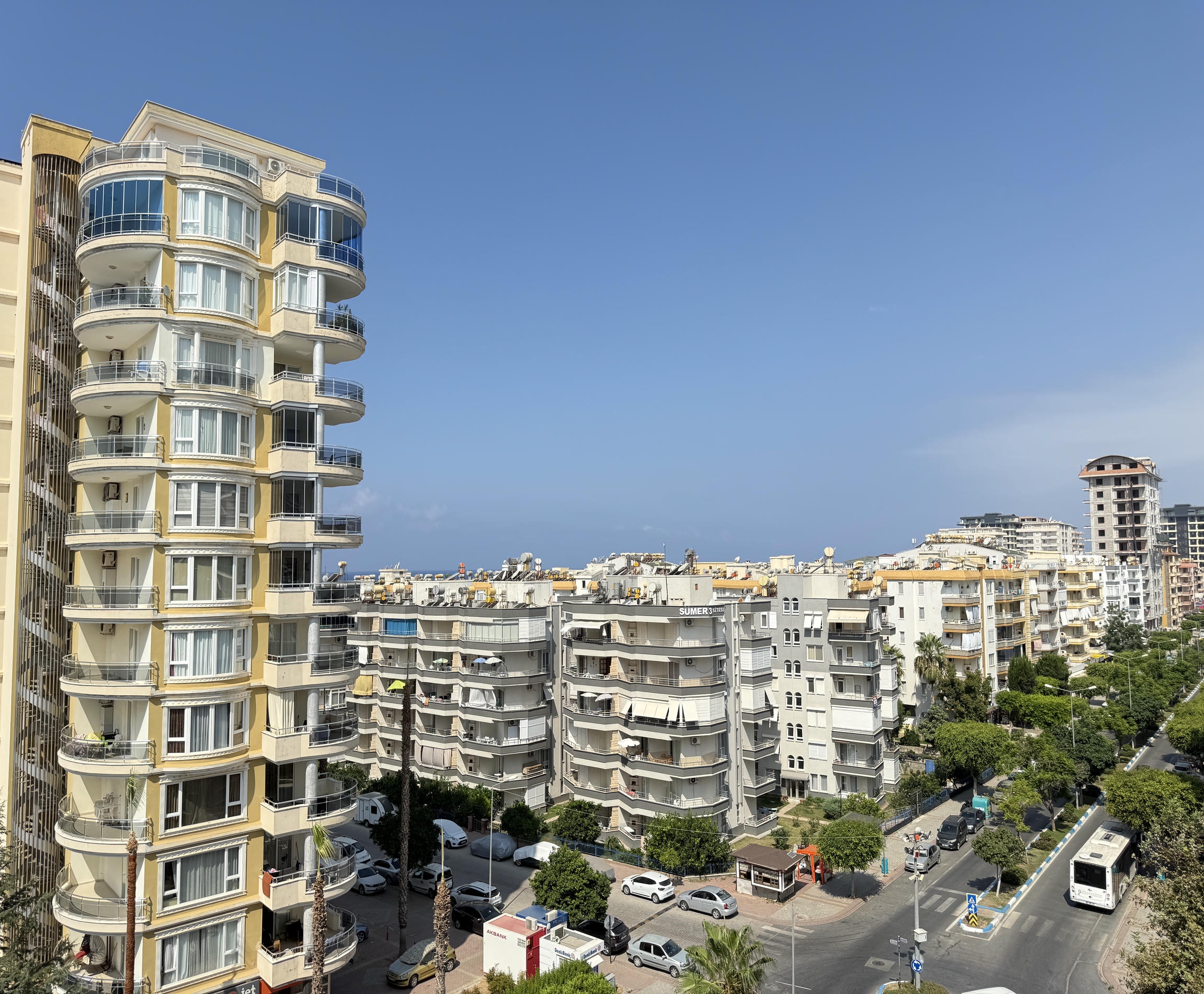 Satışta olan yüksek katlı konut kompleksinde panoramik cephe camları, palmiyeler ve şehir yolu bulunuyor