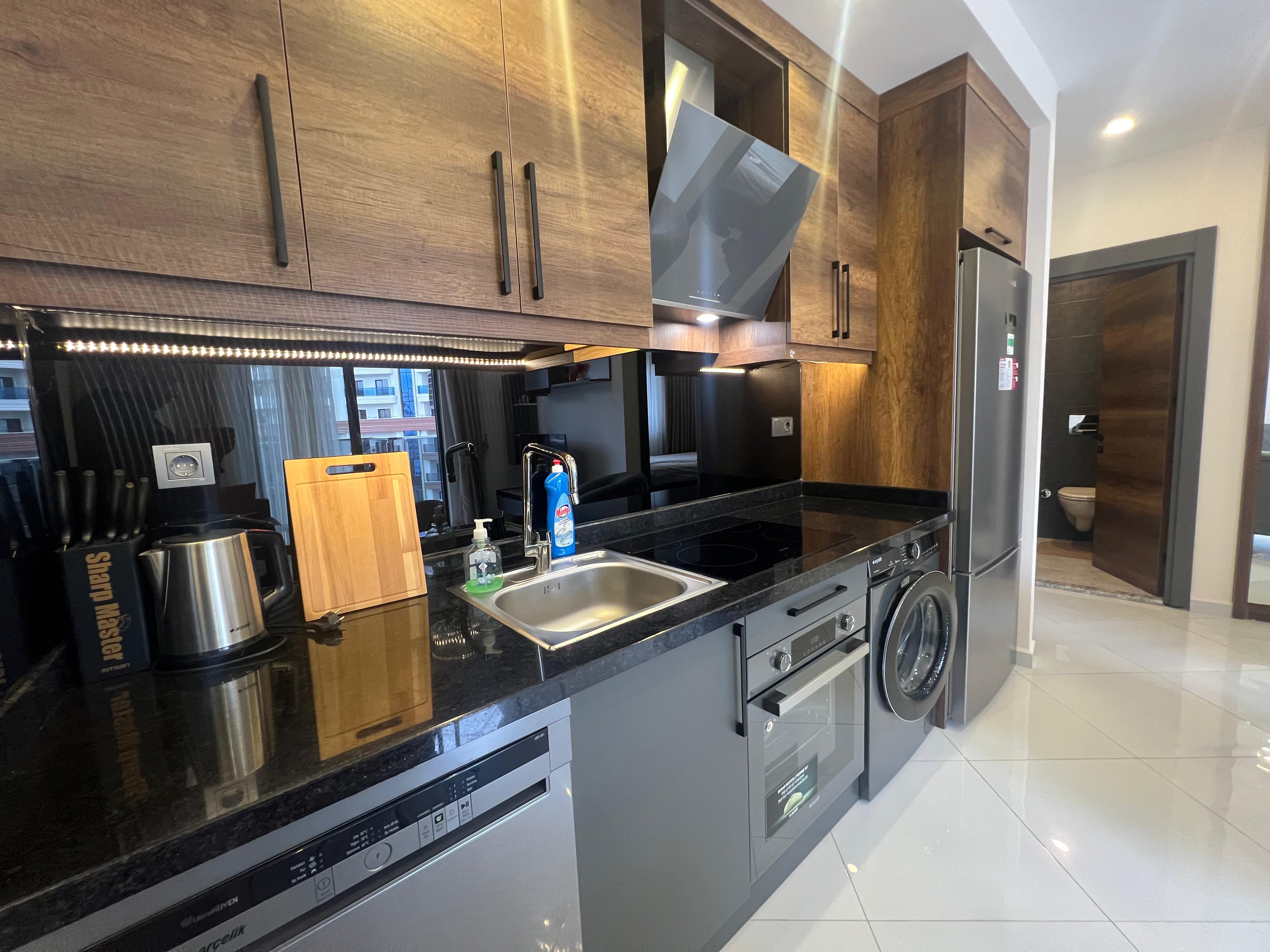 Kitchen with wood-effect cabinets and integrated appliances inside a home in Mahmutlar