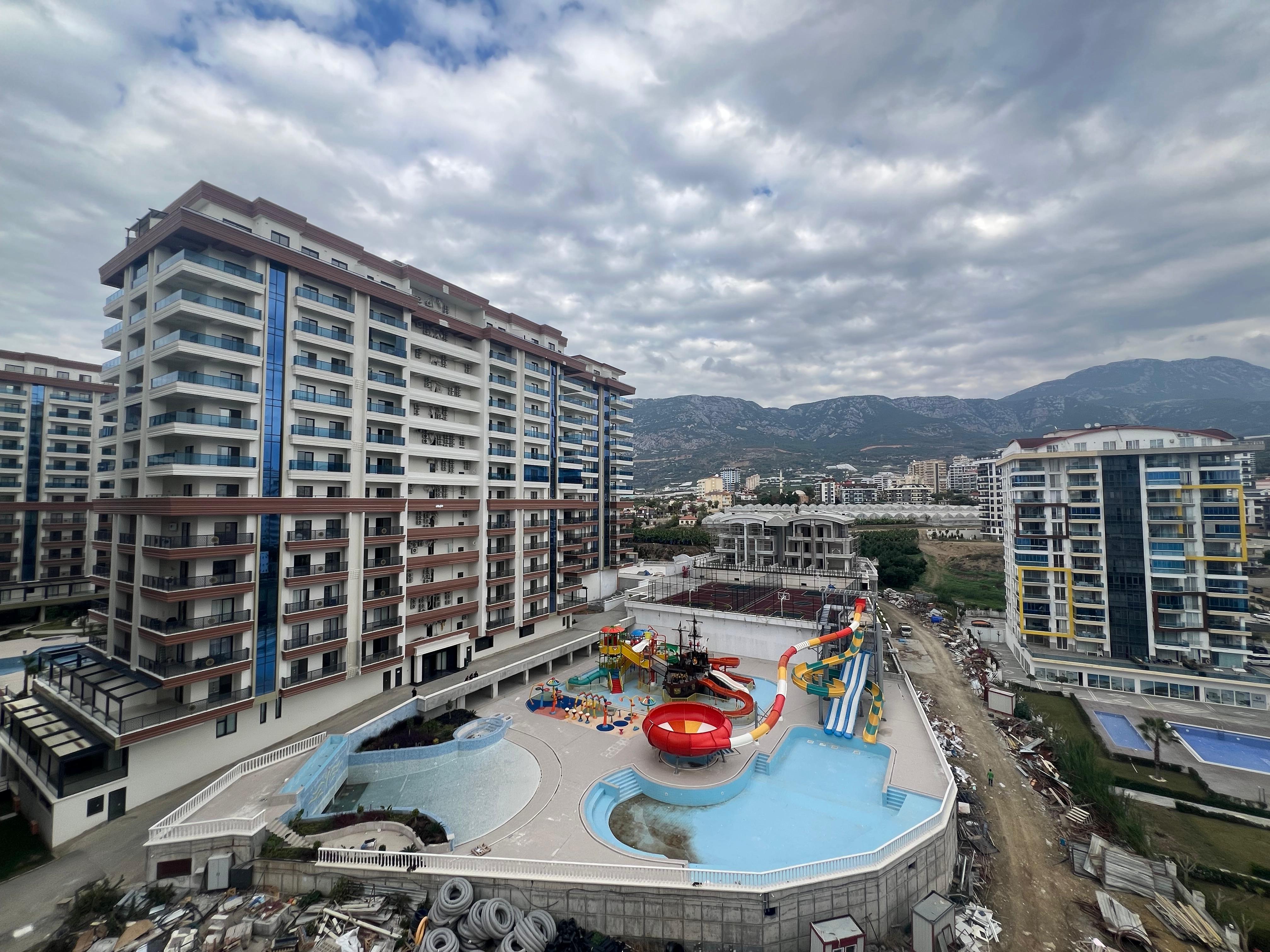 Pool with water slides and mountain ridge at a complex with apartments for sale in Turkey