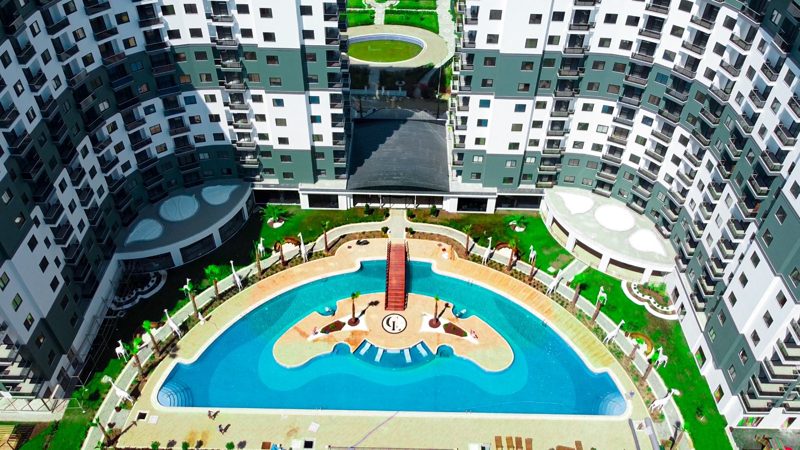 Large outdoor pool with an island and wooden bridge in a complex with apartments in Mahmutlar