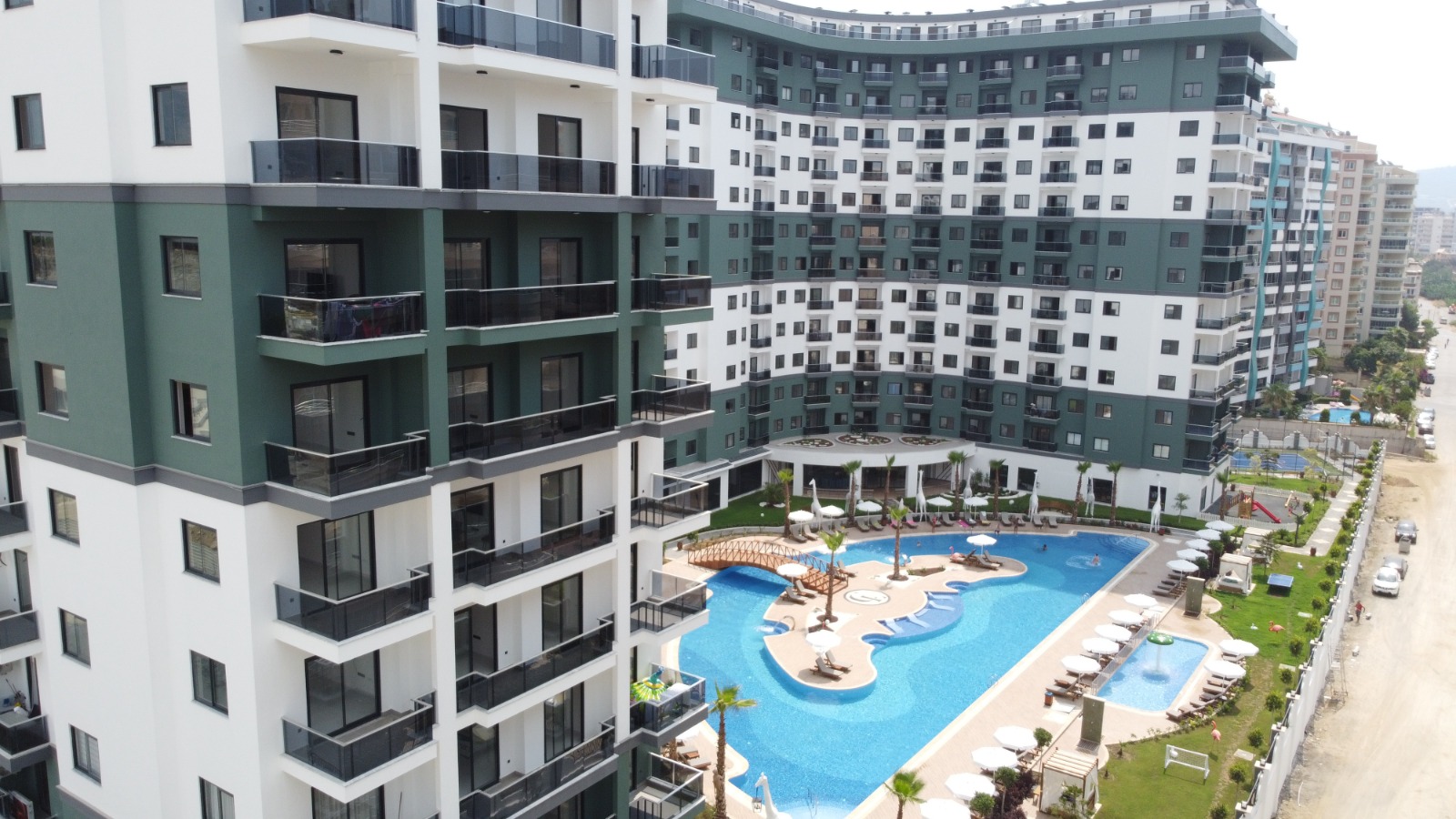 An outdoor pool with white umbrellas beside a residential facade in Mahmutlar where apartments are for sale