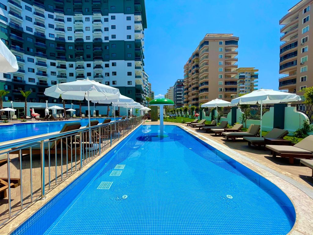 Long outdoor pool with a blue-tiled channel and white umbrellas in Turkey where apartments are for sale