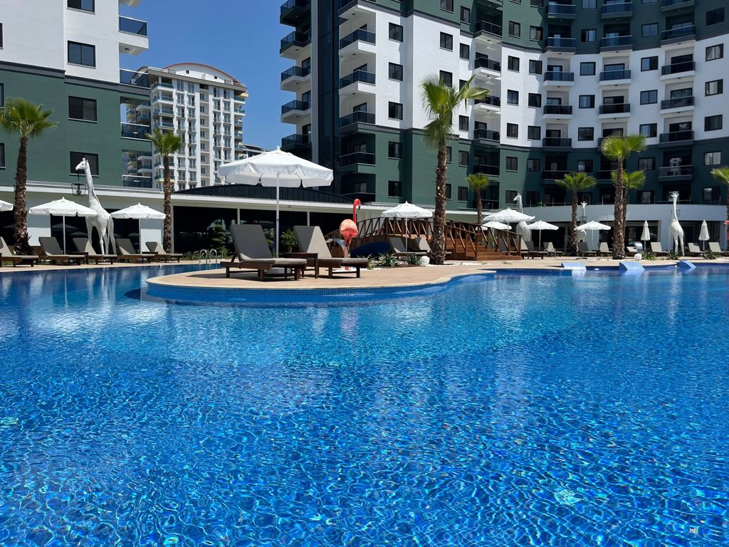 Island loungers beside a large pool with palms in a complex with apartments in Mahmutlar for sale