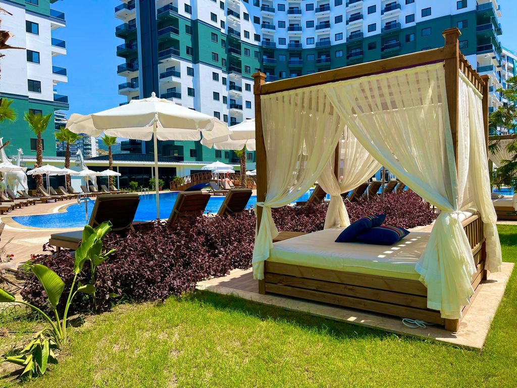 Curtained wooden gazebo beside a pool on green lawn in a complex with flats for sale in Turkey