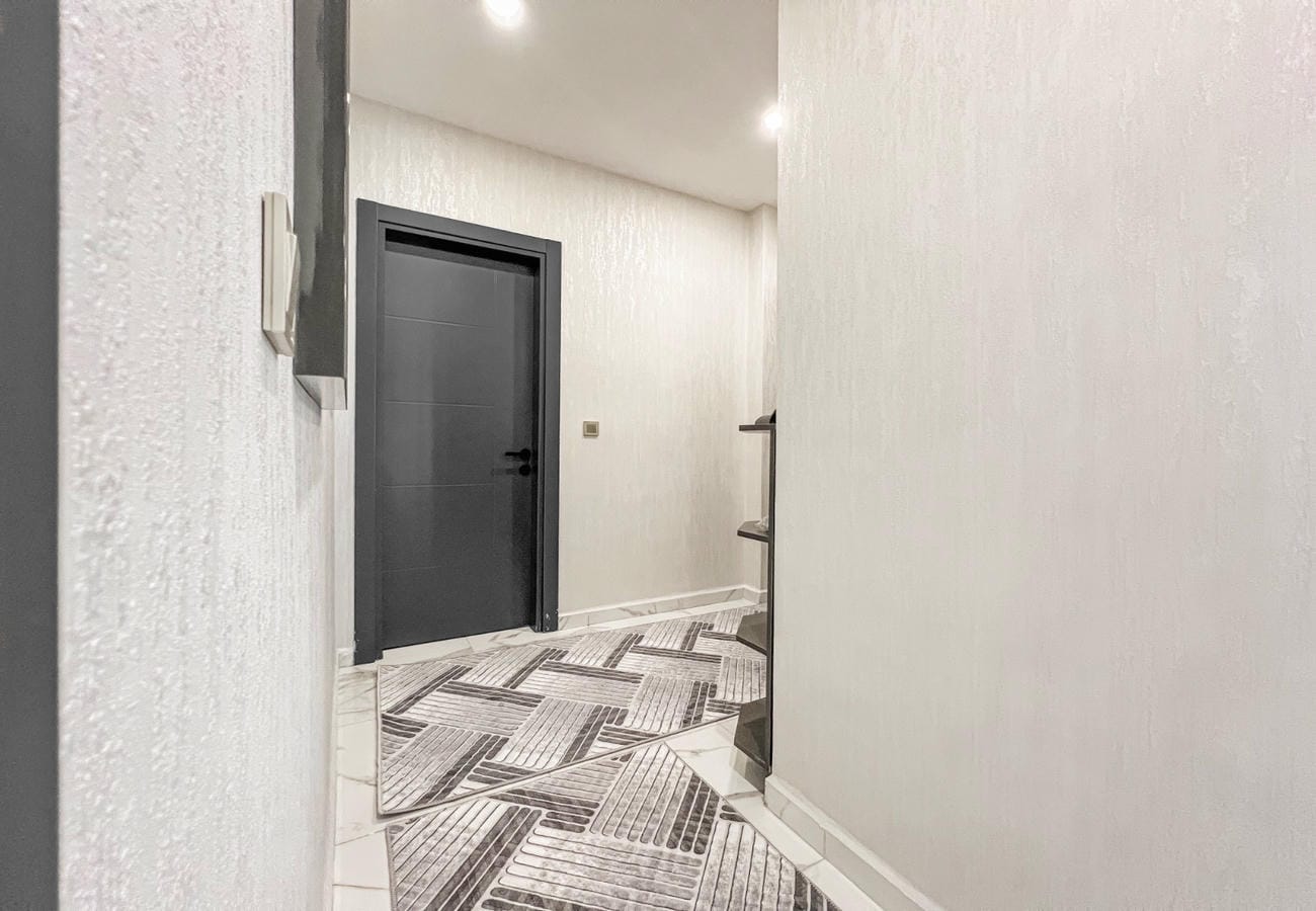 Narrow apartment corridor with black entrance door and geometric mats in Mahmutlar