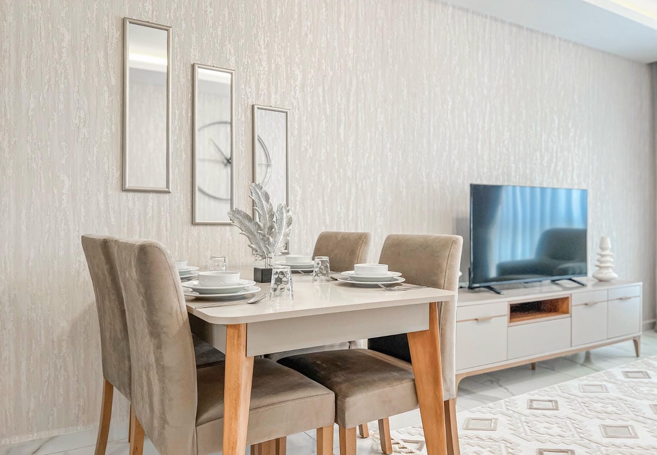 Dining area in a kitchen-living room with set table, soft chairs and television in an apartment for sale
