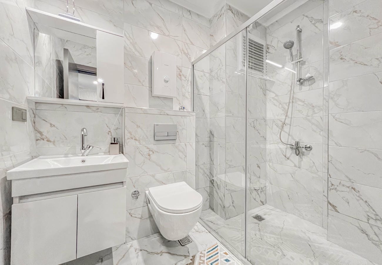 Bathroom with glass shower screen, vanity unit and marble wall and floor tile in a flat