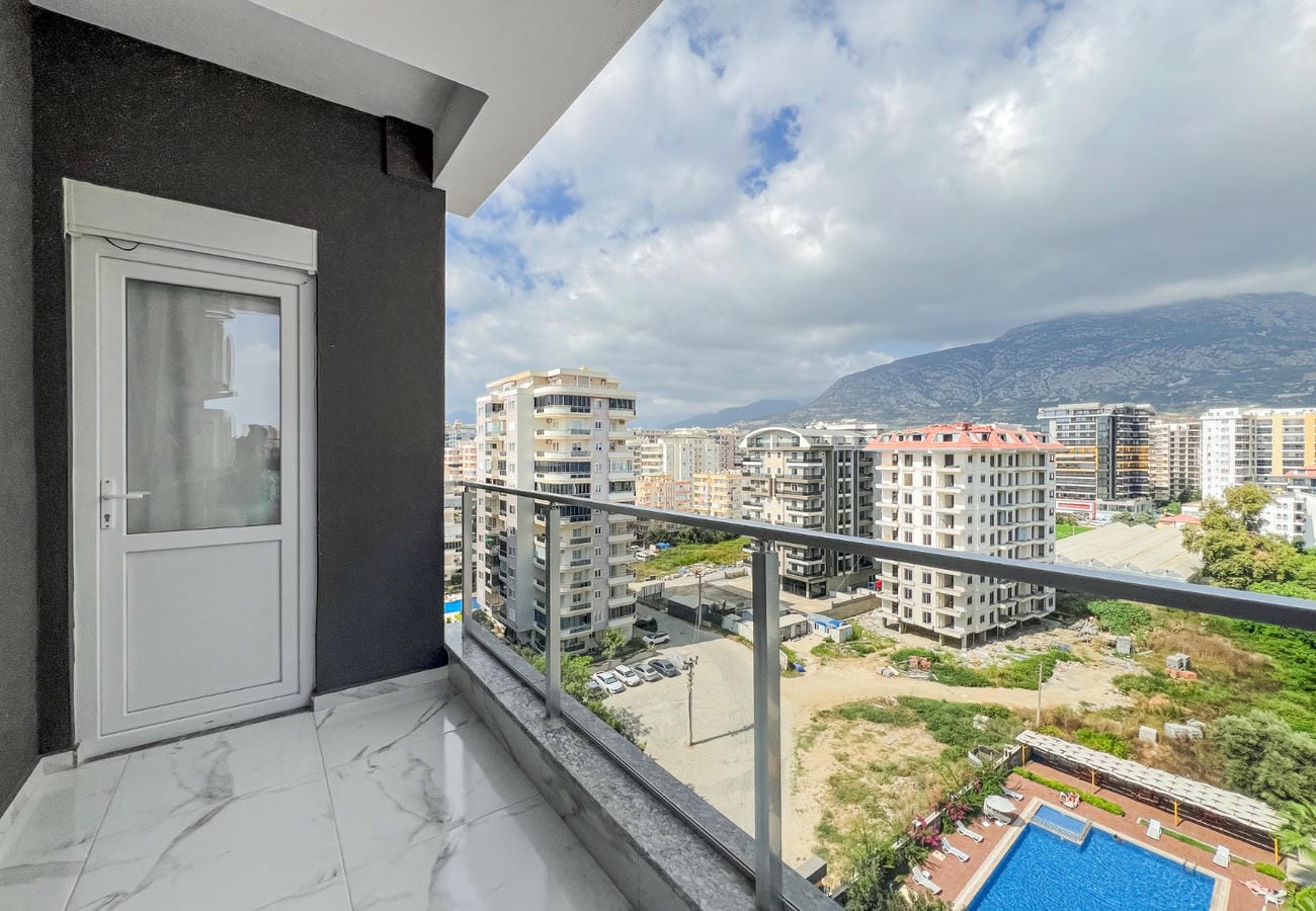 Balcony with glass railing, mountain view and pool below in a residence in Mahmutlar