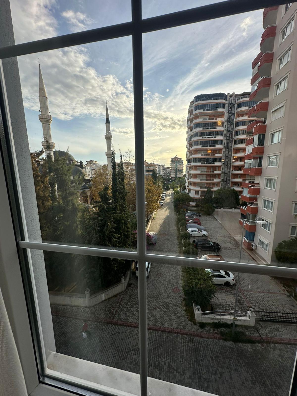 Вид из окна на городскую улицу, мечеть с двумя минаретами и жилые дома в Турции