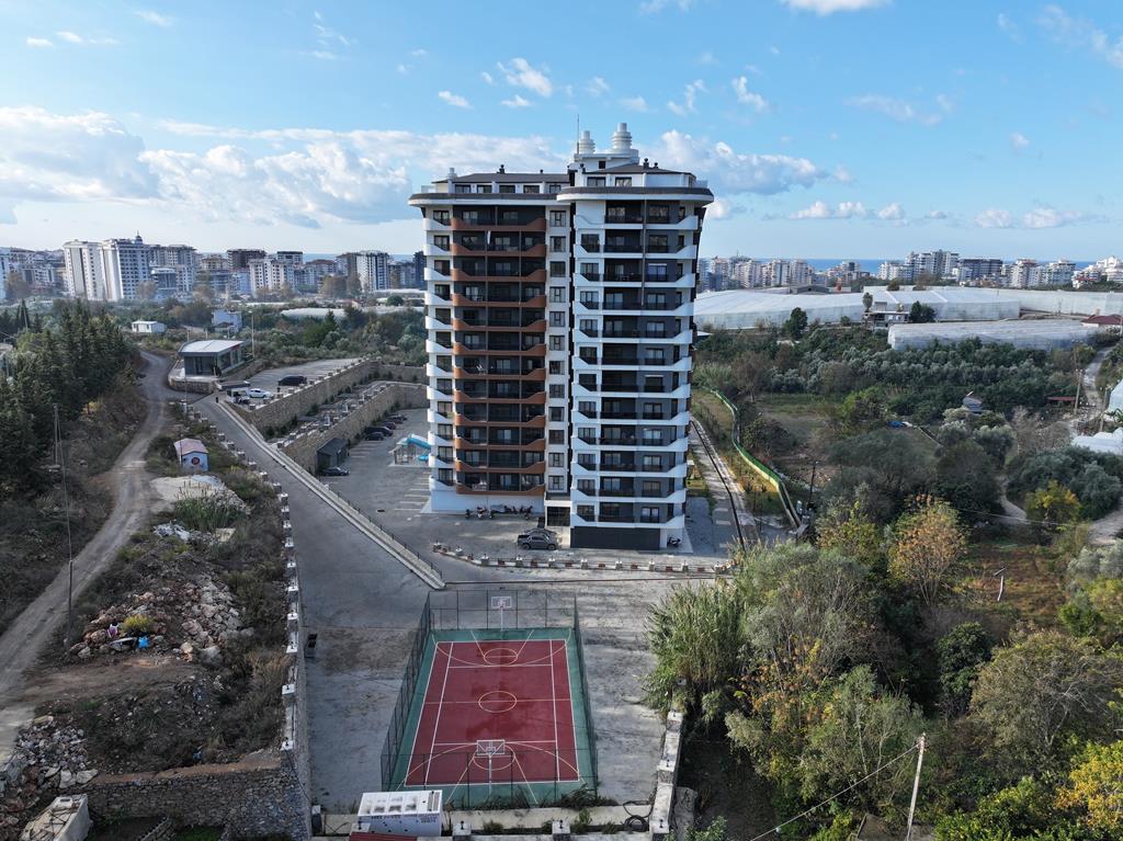 Высотный корпус у баскетбольной площадки и садовых участков в комплексе с жильём в Алании, где продаются квартиры