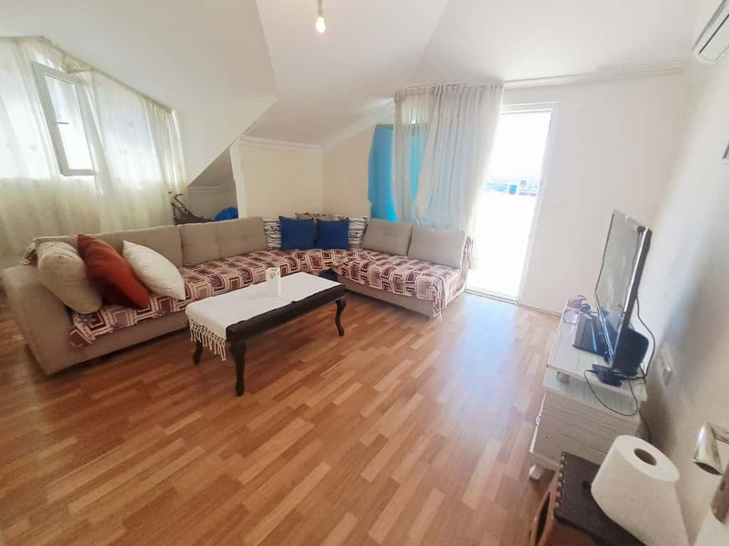 Eğimli tavanlı salonda, Türkiye'de satışta olan penthouse'un köşe koltuğu ve balkon kapısı
