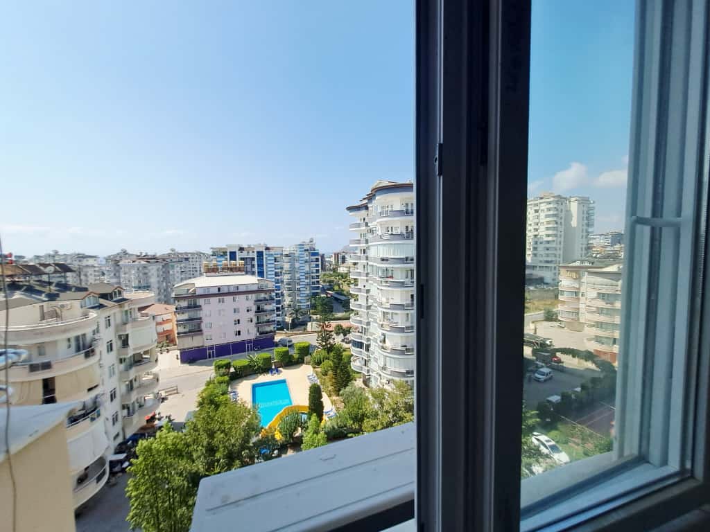 Türkiye'de penthouse'ların bulunduğu sitede açık pencereden havuz, ağaçlar ve çevredeki binalar