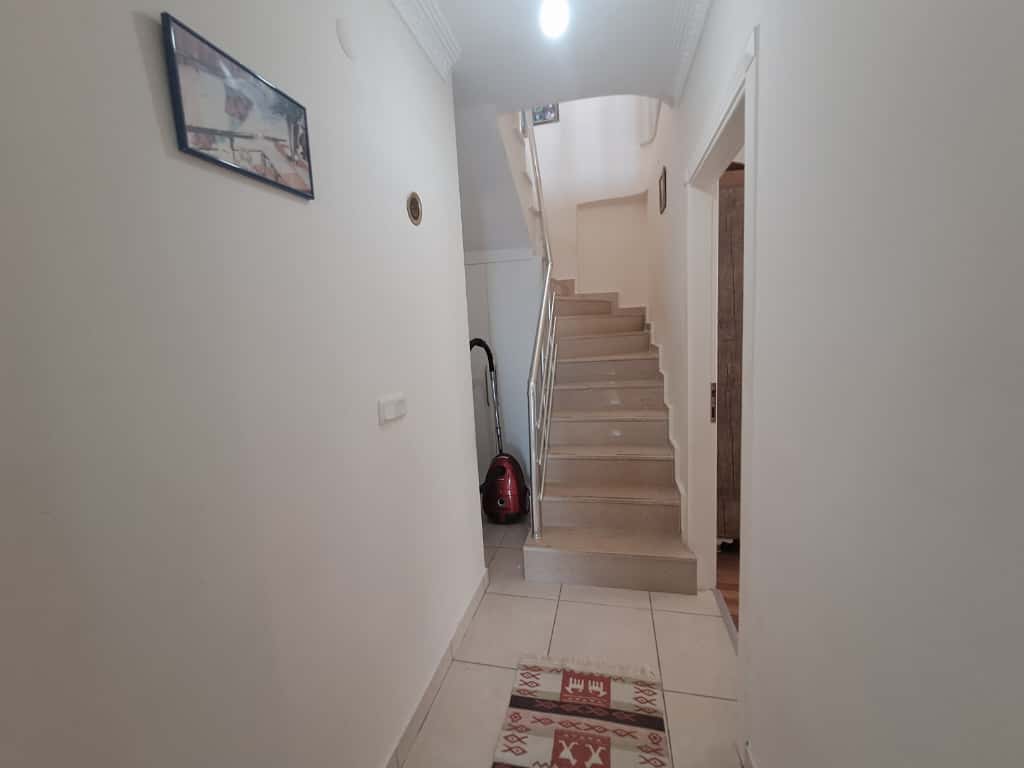 Alanya'daki penthouse'un merdiveninde bej fayanslı basamaklar, metal korkuluk ve desenli yolluk