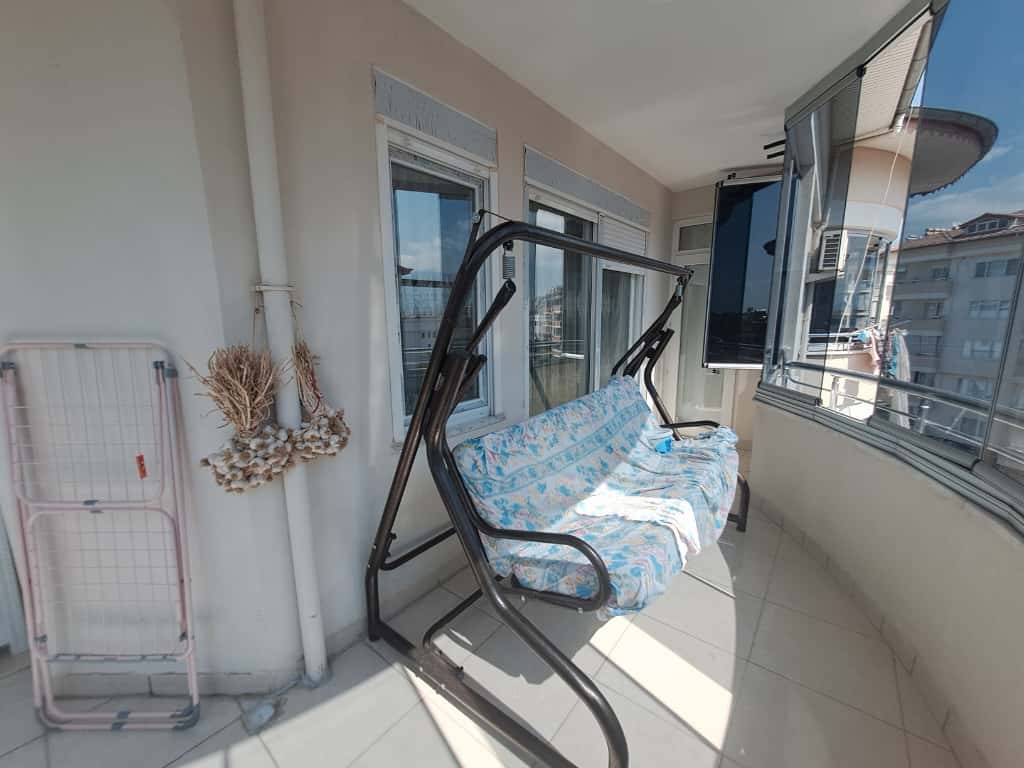 Çiçekli mavi örtülü asma salıncağın bulunduğu Türkiye'de satılık penthouse balkonunda cam korkuluk