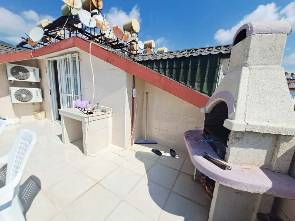 Çikcilli'de satılık penthouse'un açık terasında bacalı taş barbekü, duvar yanında eviye ve klima üniteleri