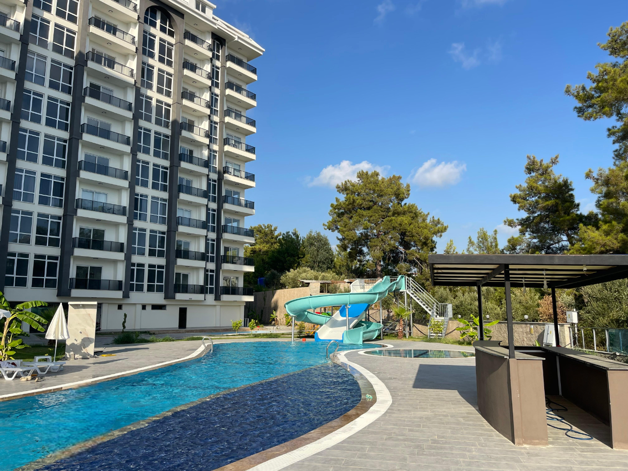 Curved outdoor pool with a turquoise slide in a complex with apartments for sale in Turkey