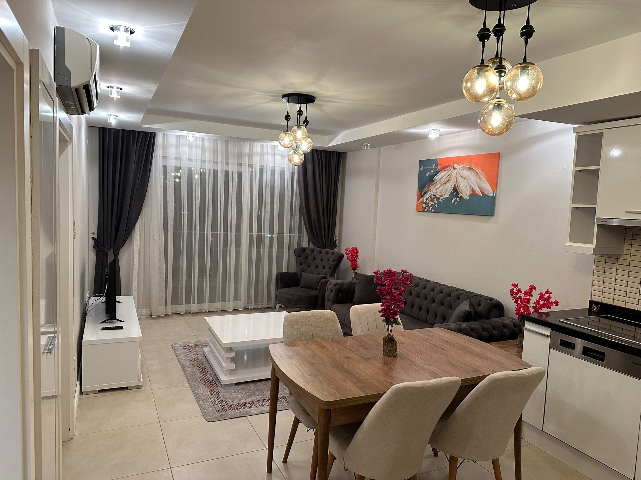 Деревянный обеденный стол и тёмно-серый диван в кухне-гостиной квартиры с вечерним видом в Джикджилли