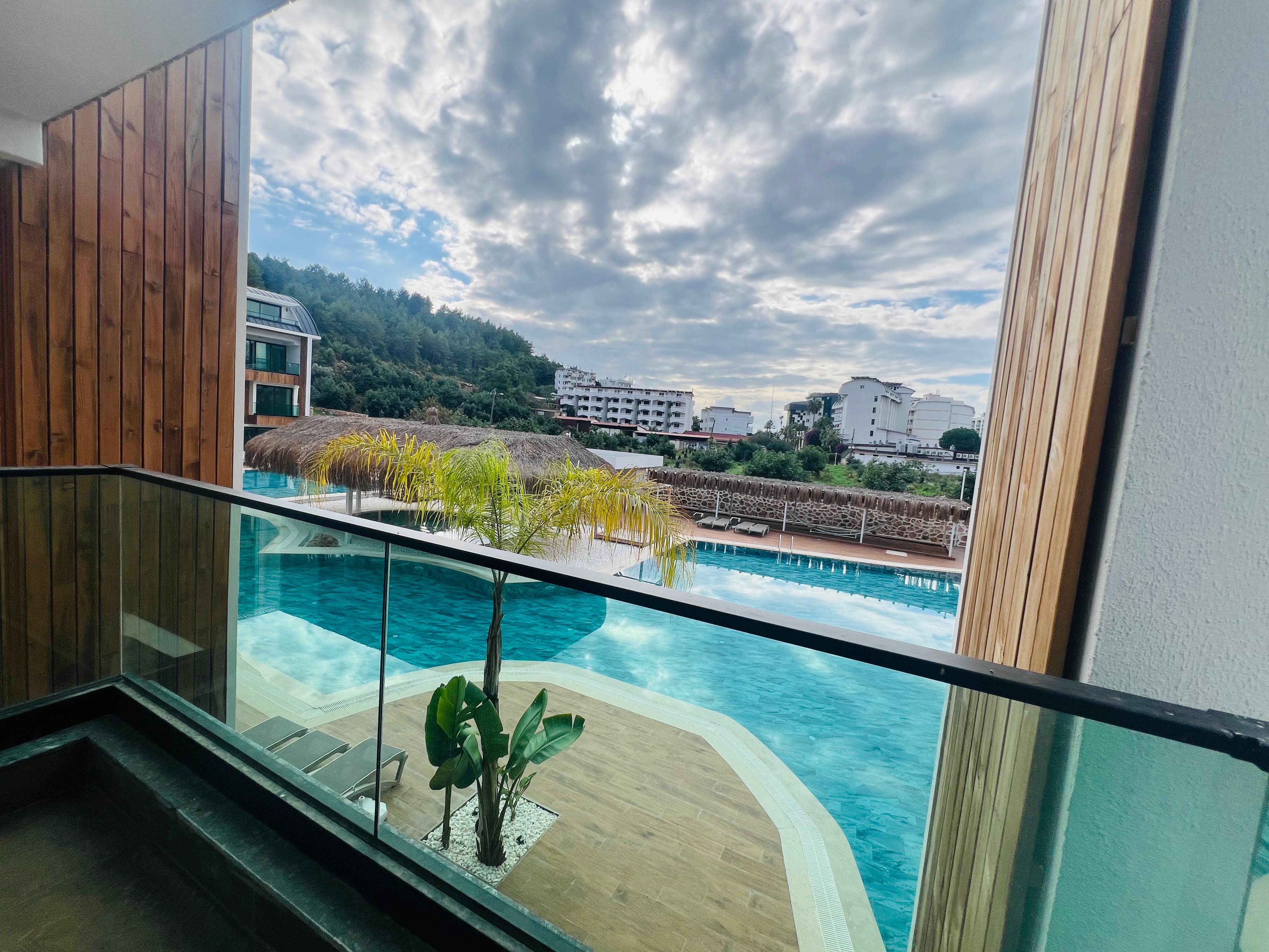 Havuza bakan cam korkuluklu balkon satılık evin ahşap duvarları önünde