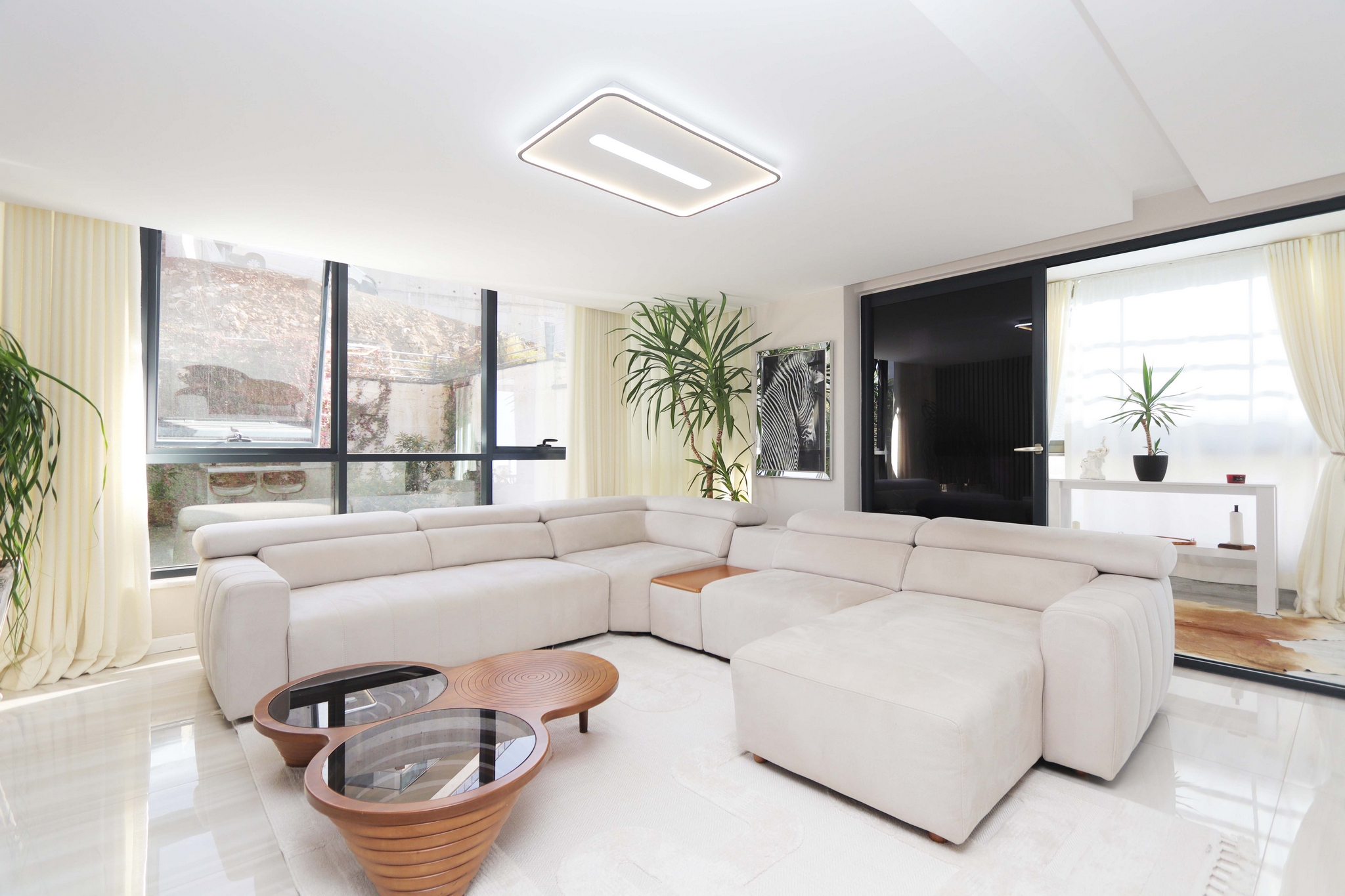 Living room with a corner sofa, panoramic windows and round tables in a 2+1 apartment for sale