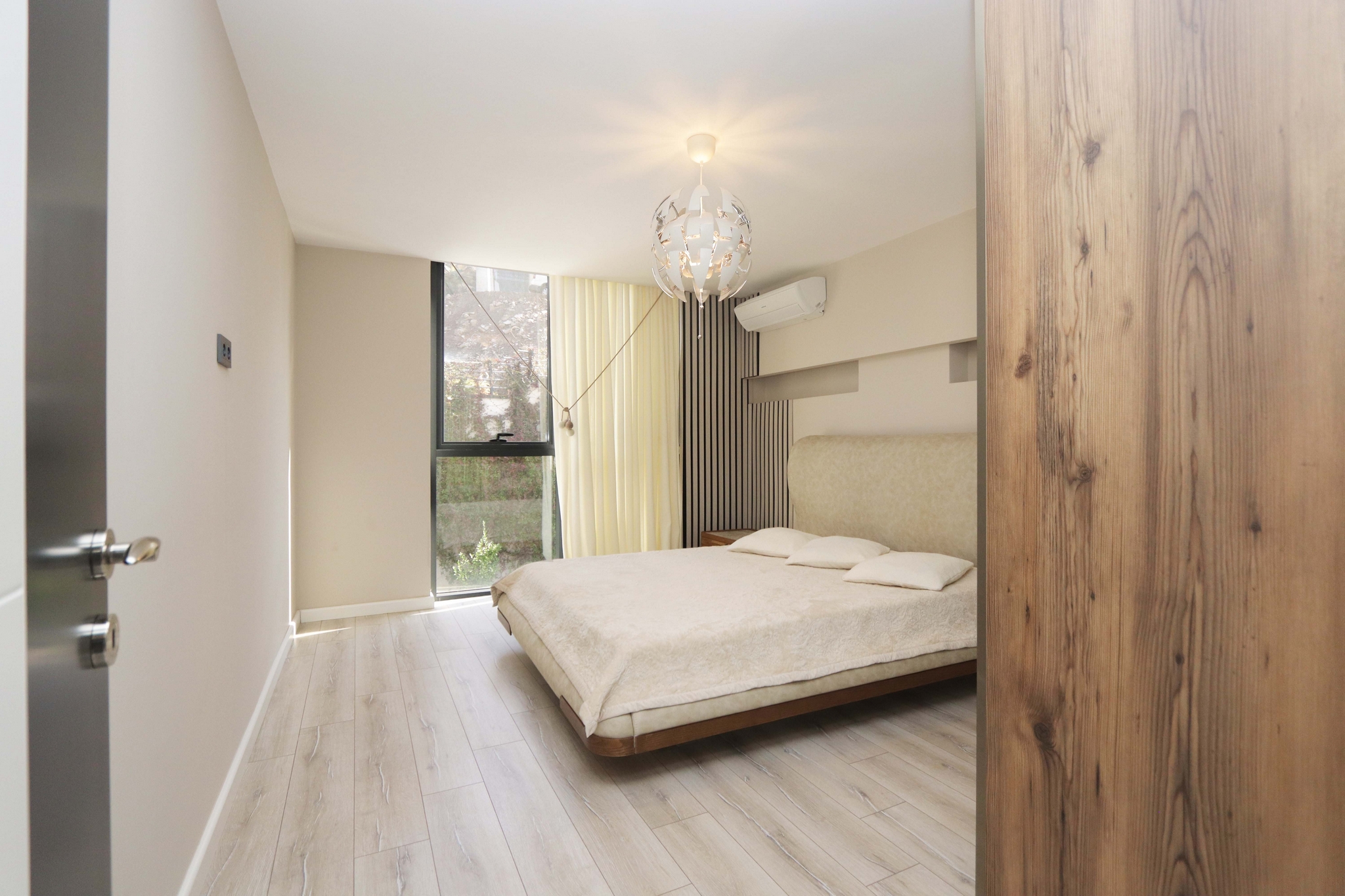 Bedroom with a beige-covered bed, panoramic window and light wooden floor
