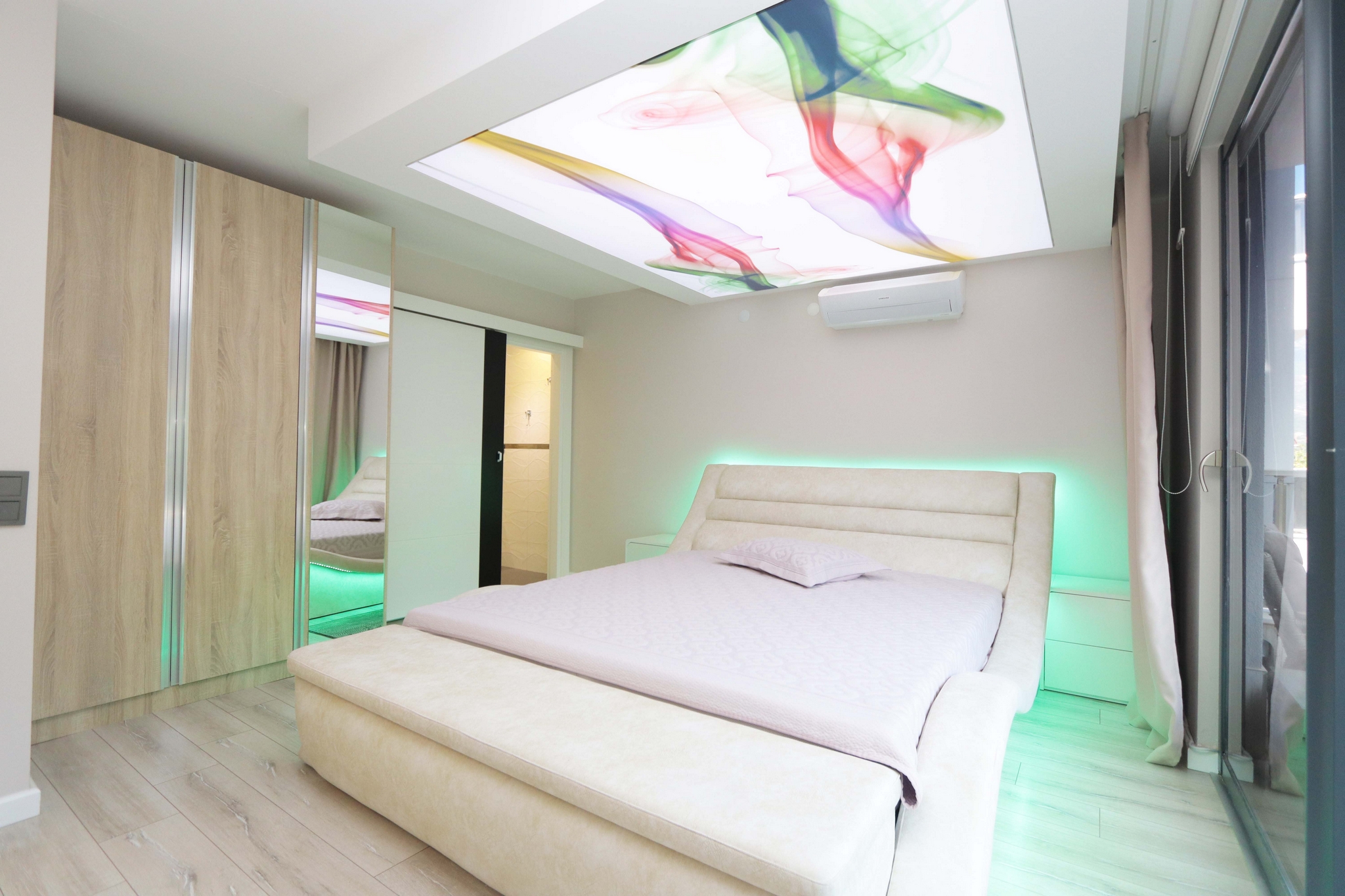 Bedroom with an upholstered headboard, mirrored built-in wardrobe and panoramic glazing in an apartment