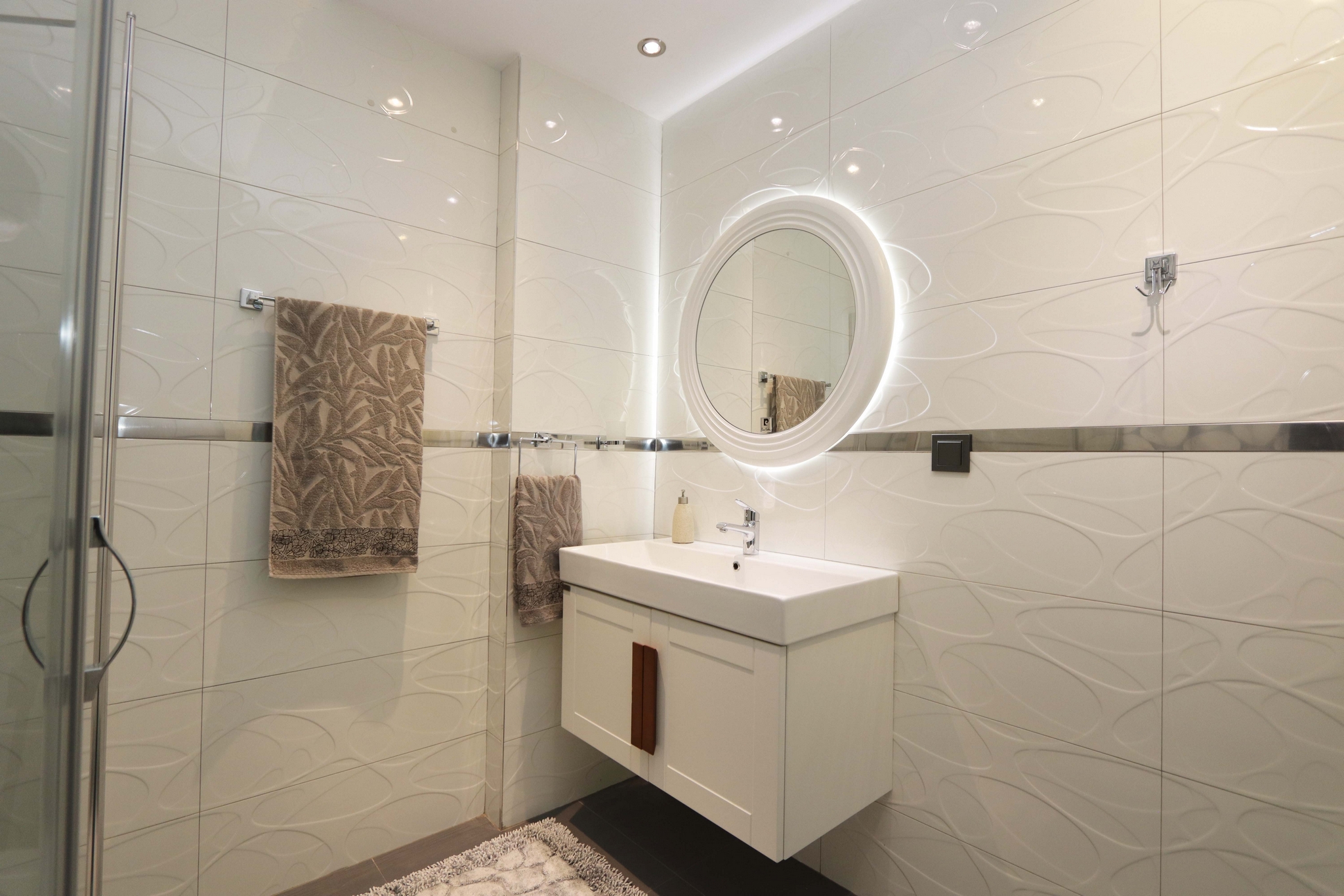 A bathroom with a glass shower enclosure, white vanity and textured wall tile in a flat