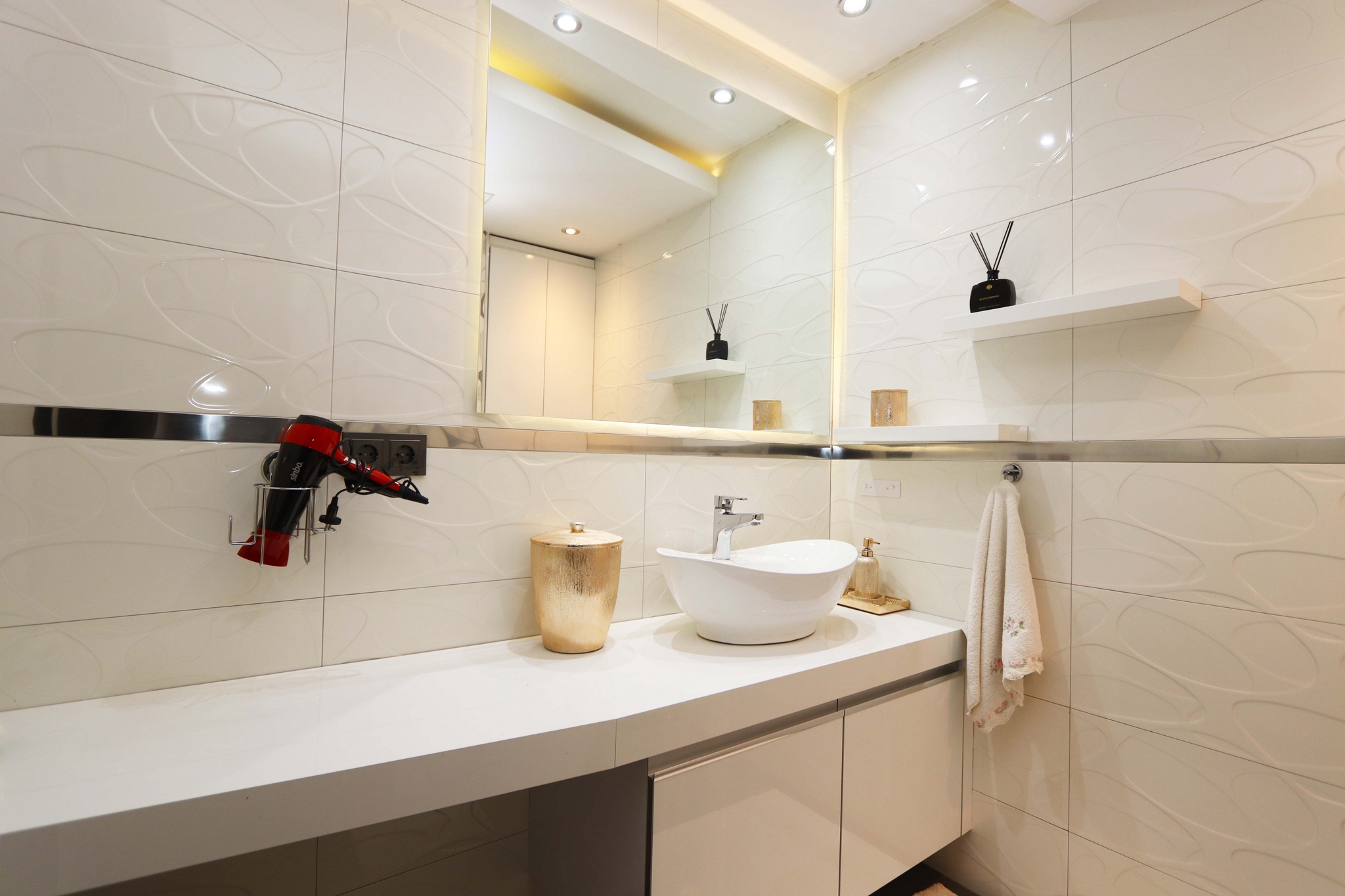 A bathroom with a white vessel sink, large wall mirror and mounted hairdryer beside textured tile