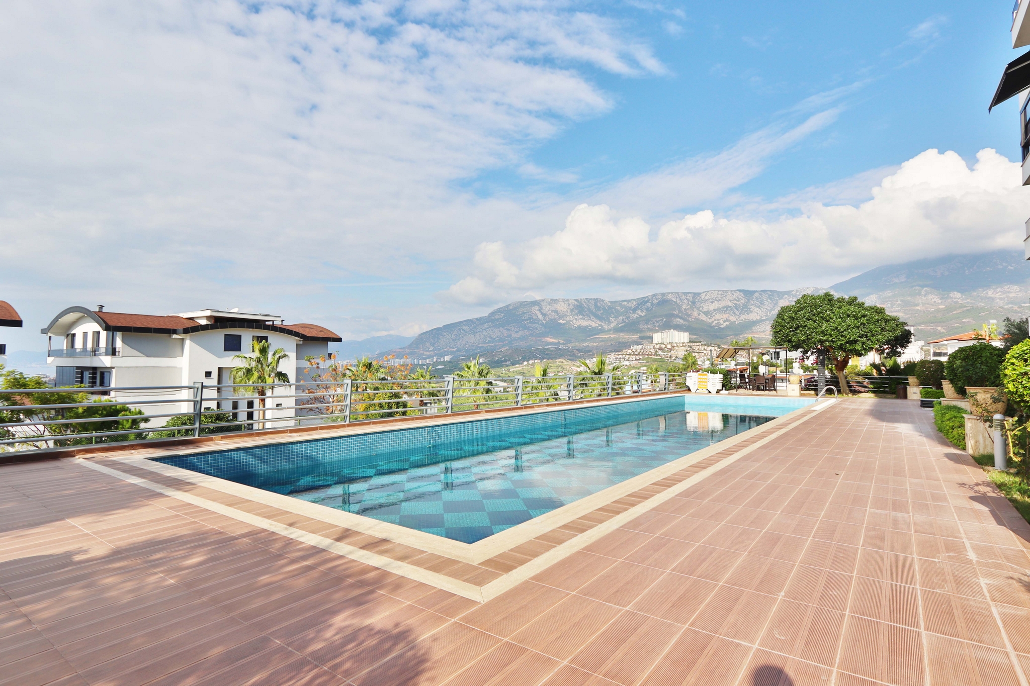 Outdoor pool with palms, tiled terrace and mountain scenery on the grounds of a residence with apartments in Kargicak, Turkey