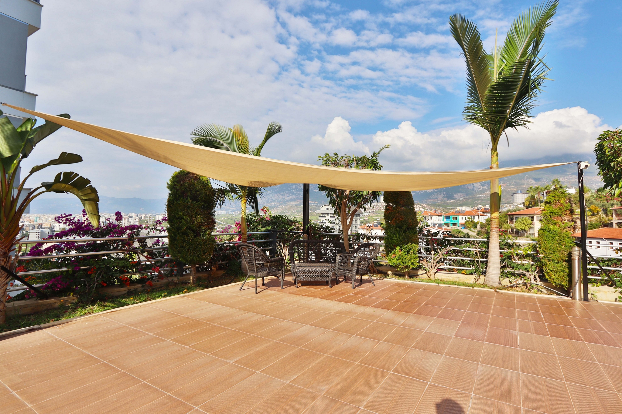 Spacious tiled terrace with a shade sail, outdoor dining set and mountain views beside an apartment for sale in Turkey
