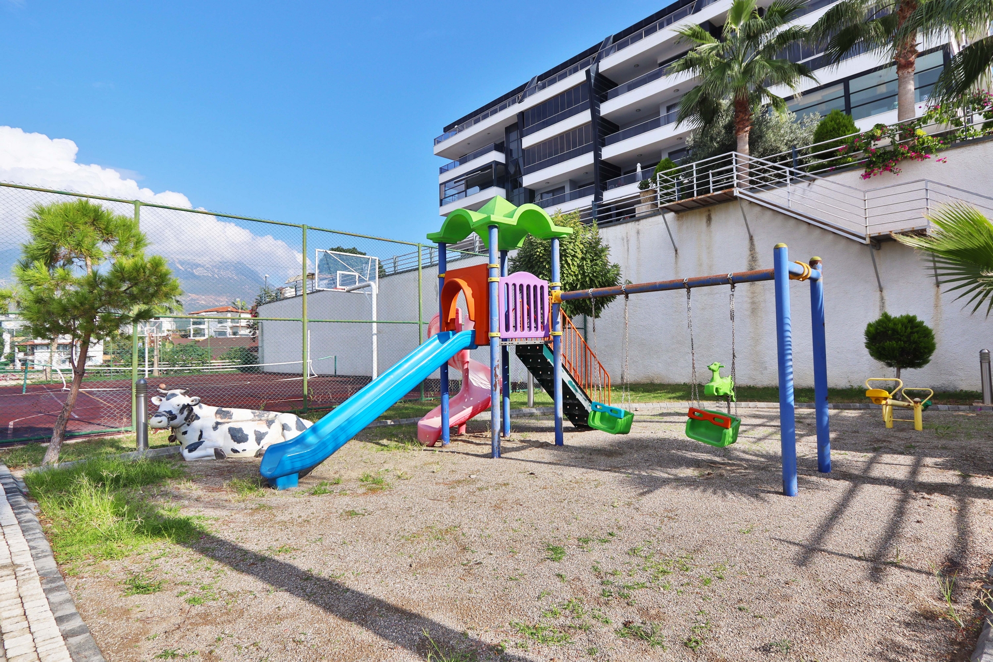 Children’s play area with a slide, swings and basketball hoop on the grounds of a complex with flats