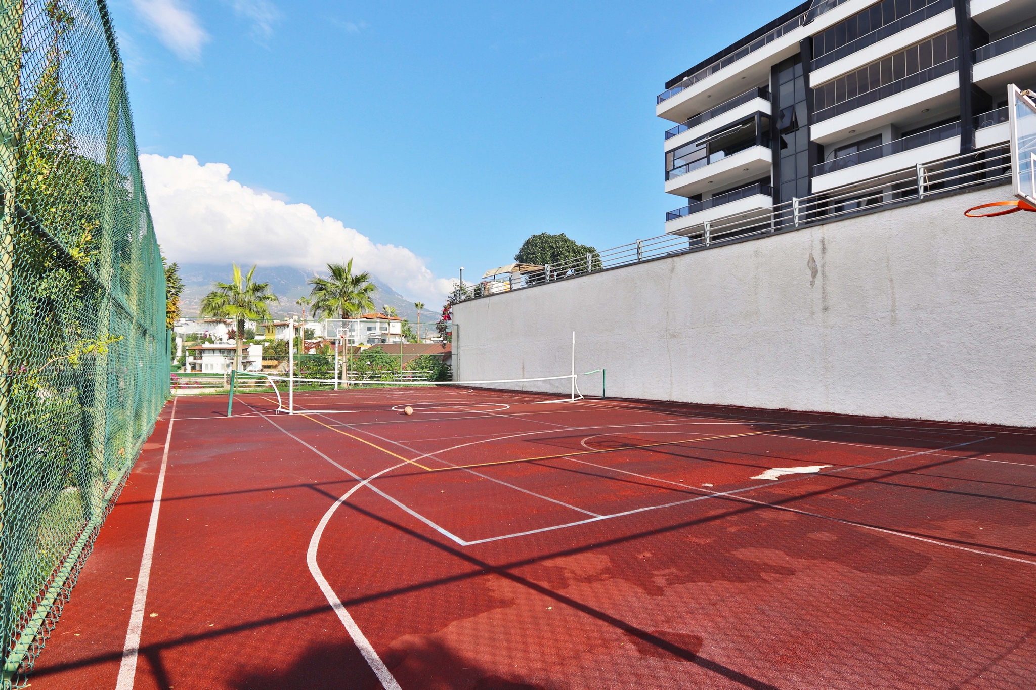 Outdoor sports court with basketball markings and mesh fencing for residents of apartments