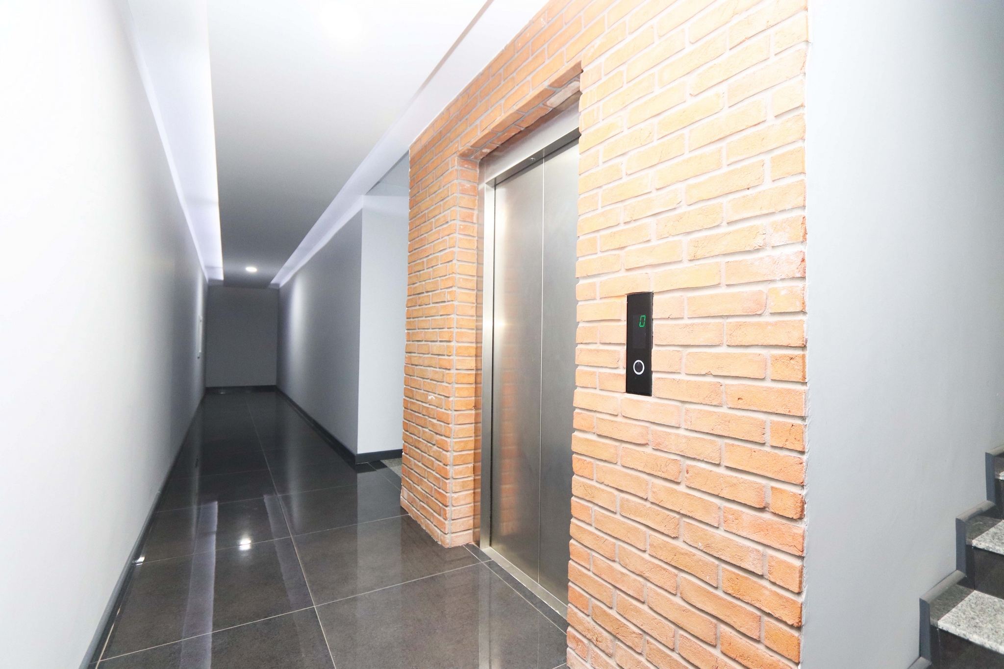 Corridor with metal lift doors, brick cladding and a staircase in a complex with apartments