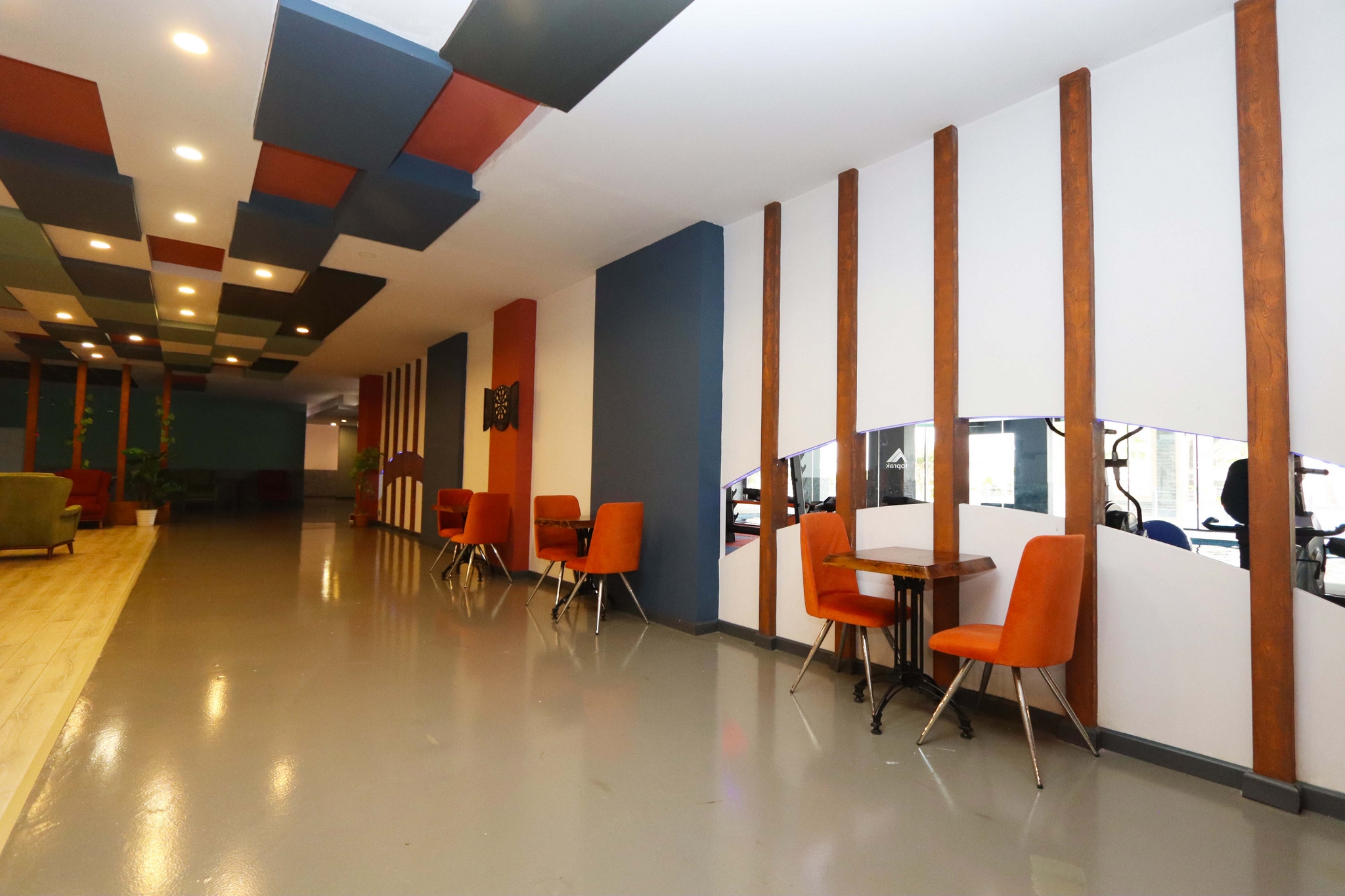 Shared space with orange chairs, a mirrored wall, gym equipment and colorful ceiling panels