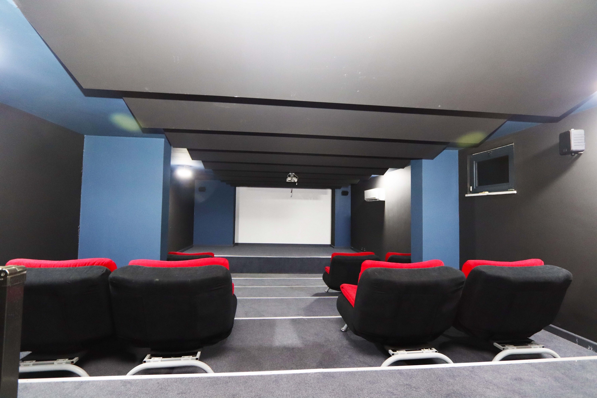 Cinema room with rows of red-headed seats, a screen and stepped floor in a complex with flats