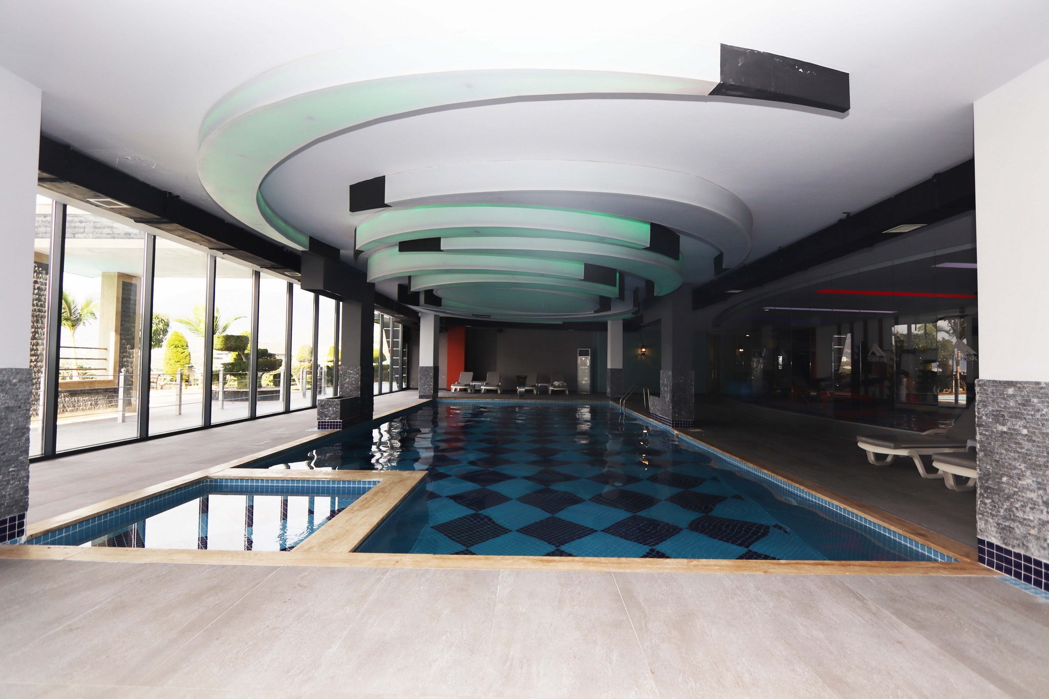 Indoor pool with mosaic tiling, loungers and panoramic glazing for apartments for sale