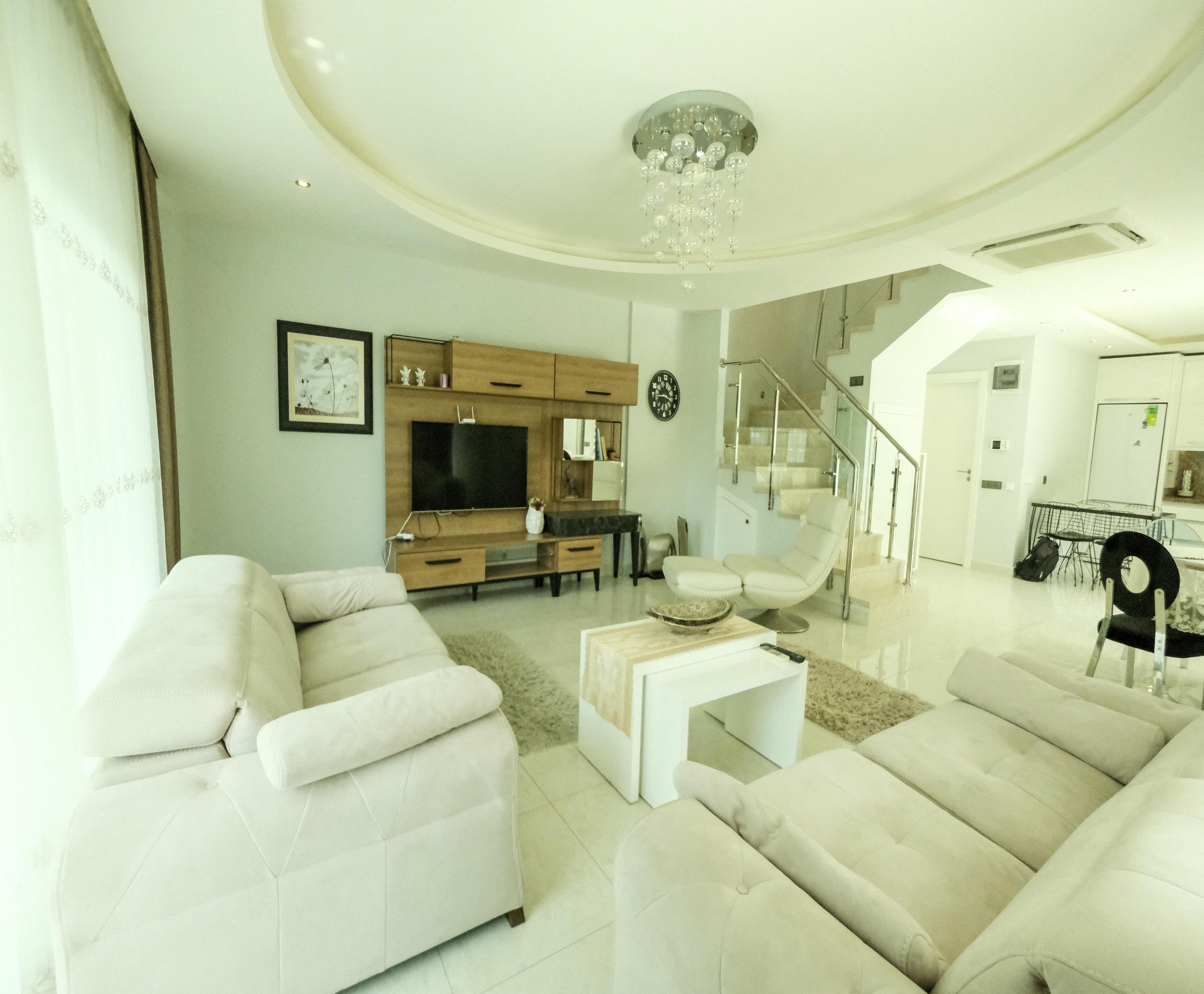 Kitchen-living room with a white corner sofa and glass-railed stairs in a 3+1 apartment for sale