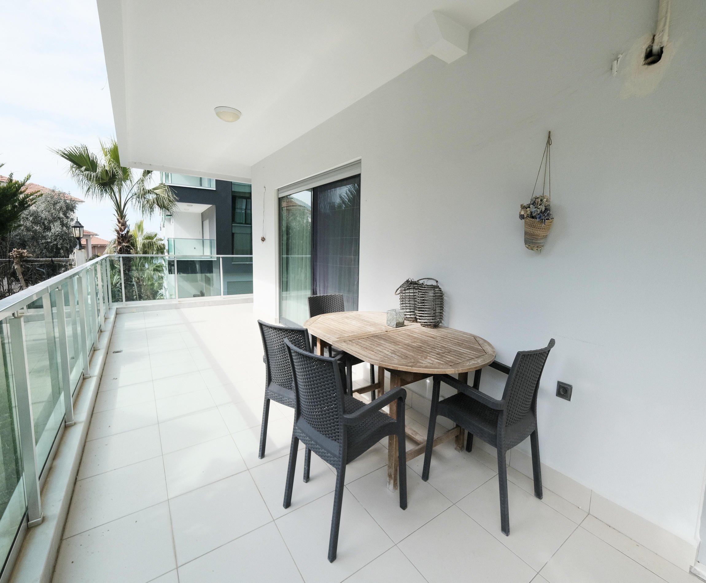 Covered terrace with a wooden table and palms beyond the railing at an apartment in Turkey