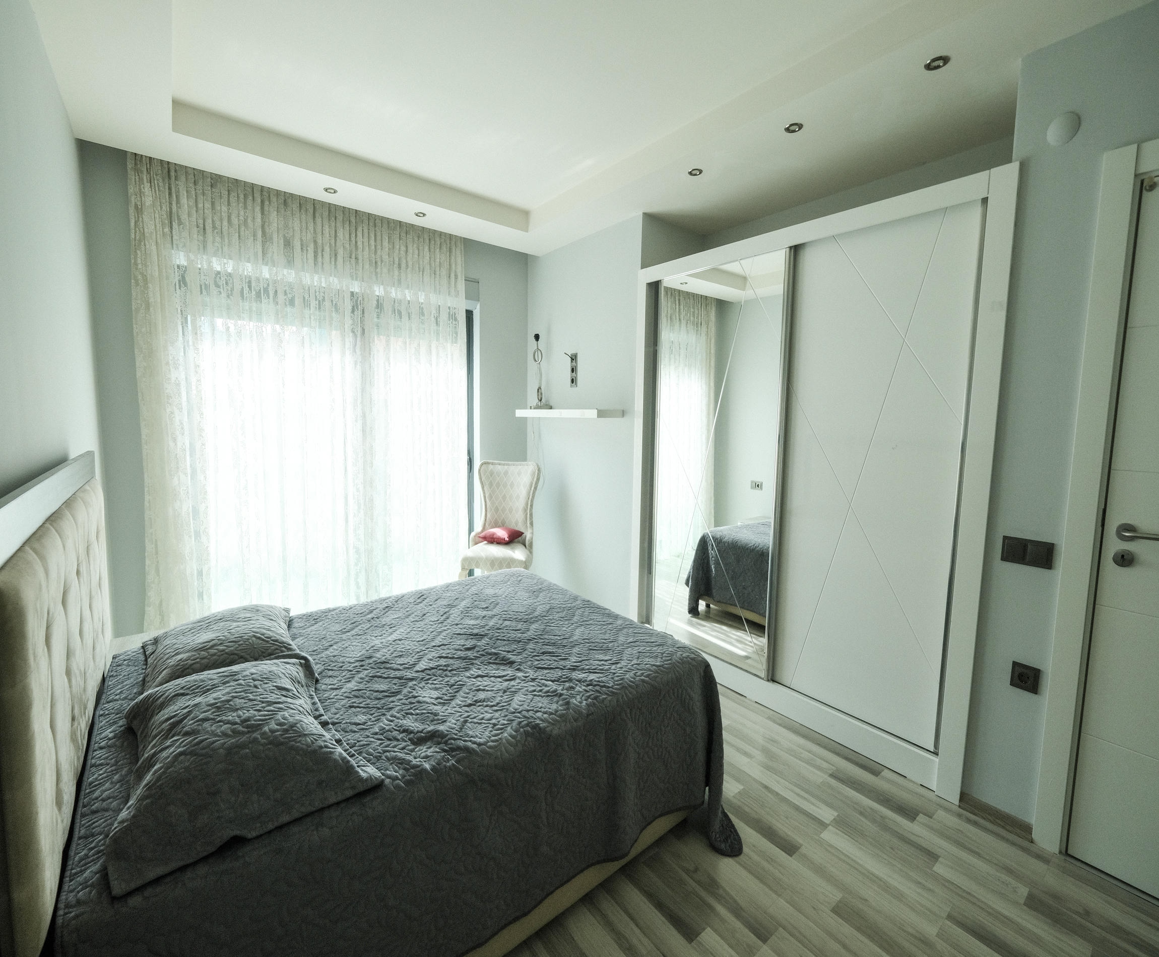 Bedroom with a double bed, mirrored wardrobe and armchair beside a curtained window