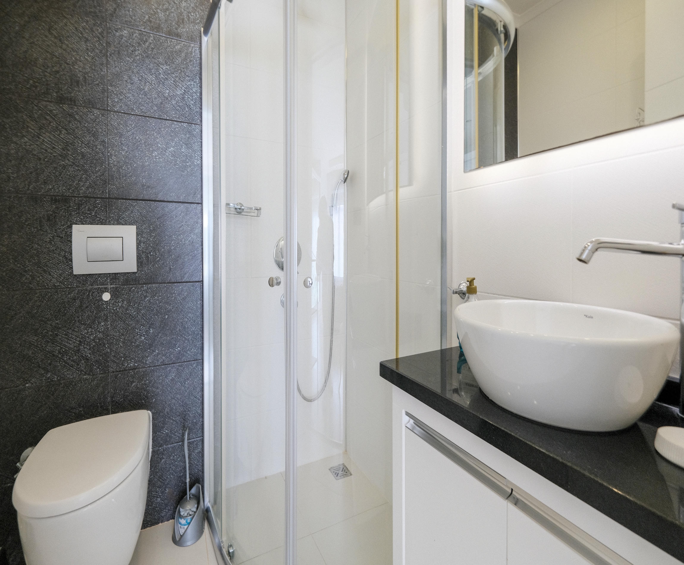 Bathroom with a glass shower enclosure and black countertop in Kargicak