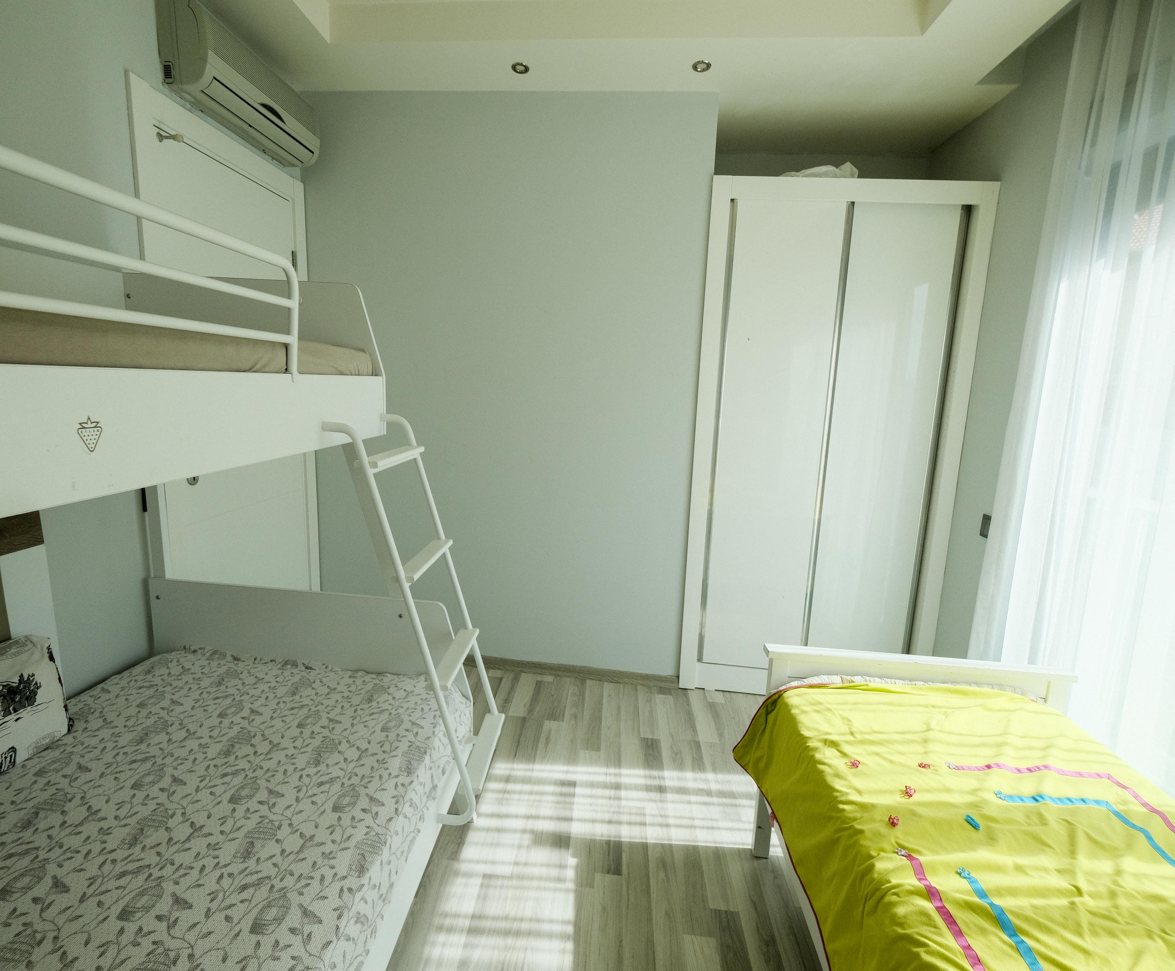 Children's room with a white bunk bed, single bed and wardrobe beside a panoramic window