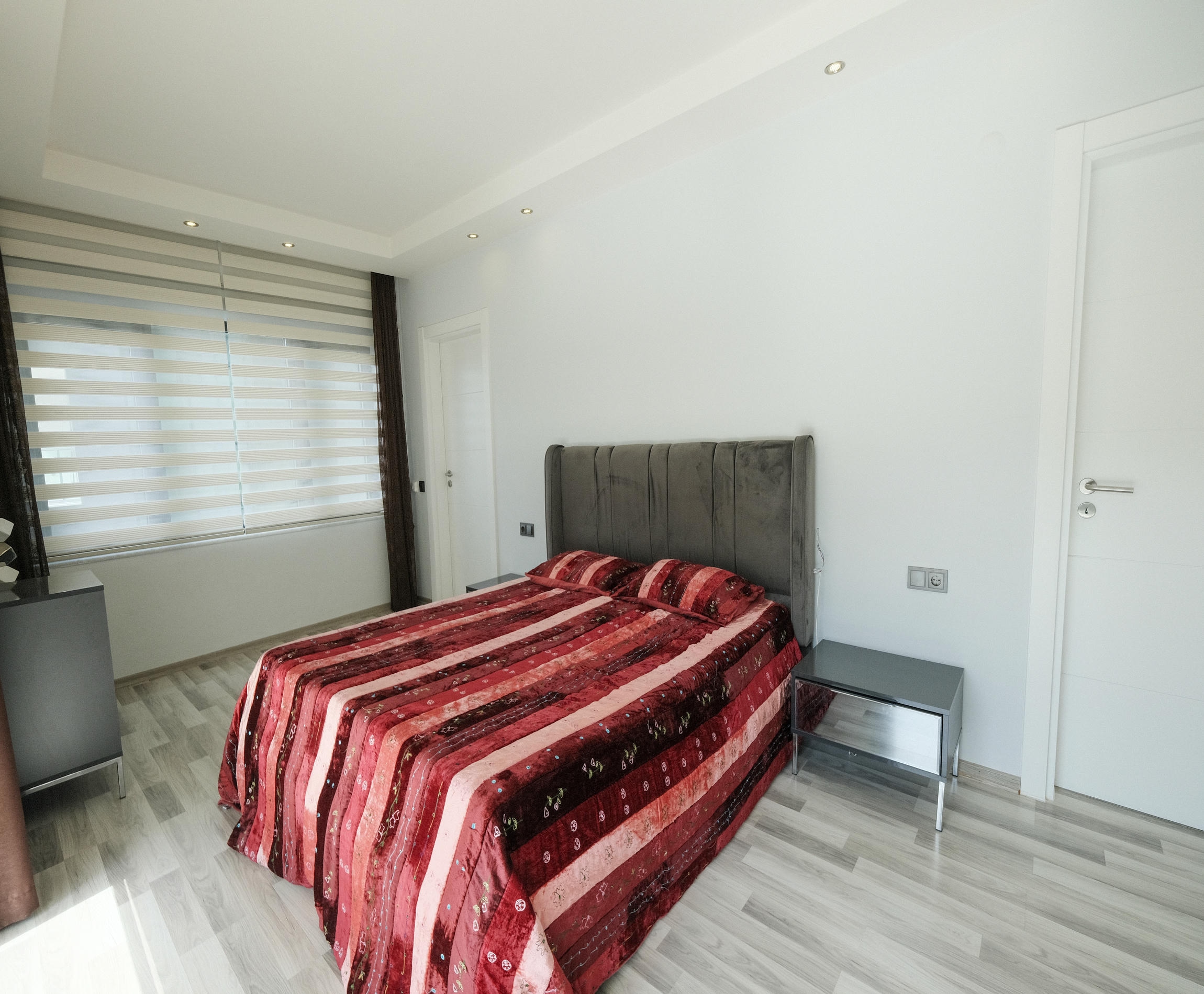 Bedroom with a double bed covered in red stripes and two bedside tables in an apartment