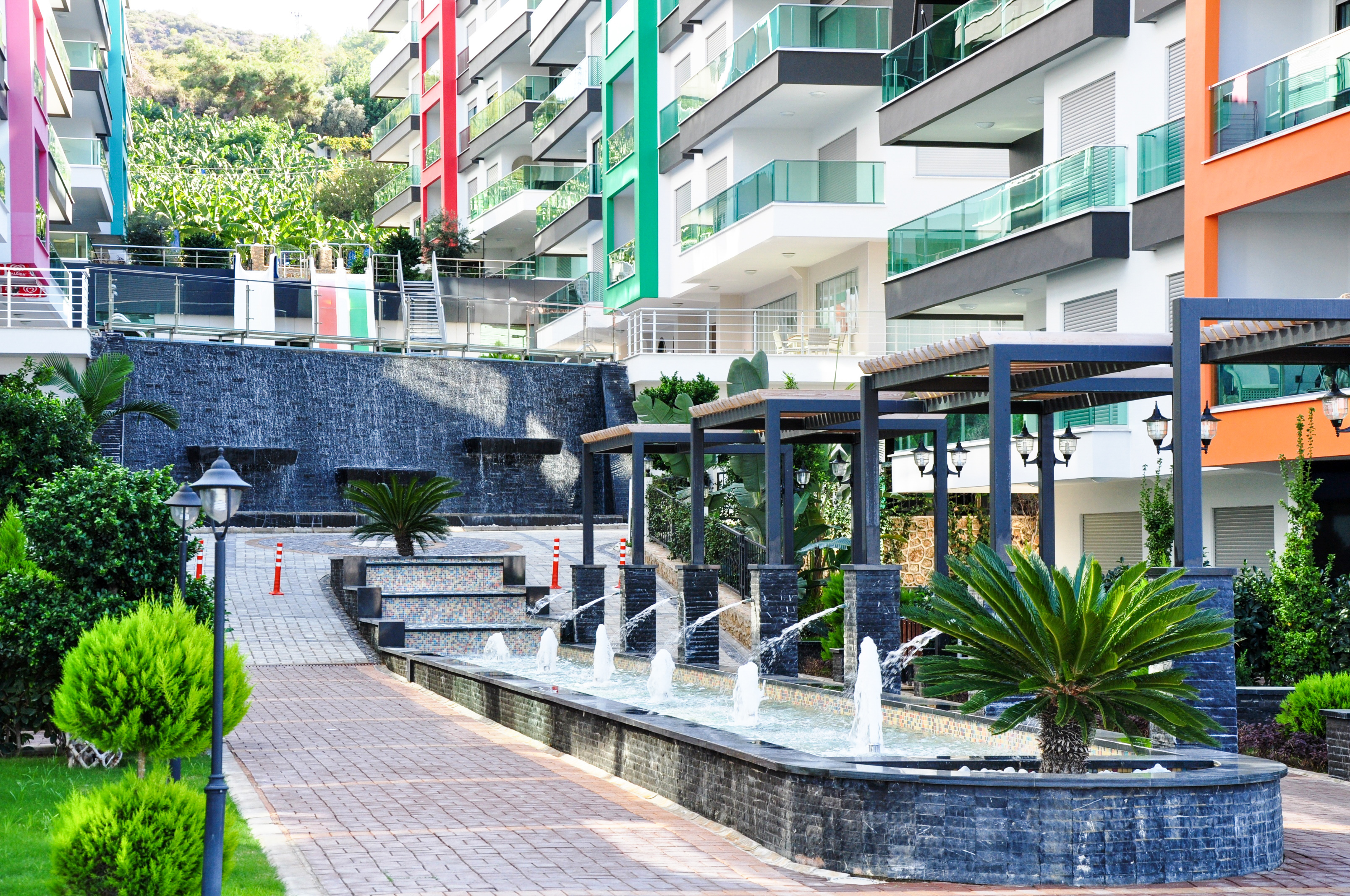 Cascading fountain with stone bowls and a pergola among apartment buildings in Turkey where apartments are for sale
