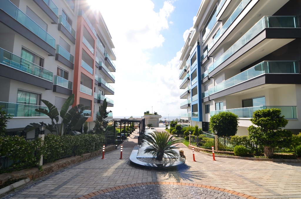 Paved walkway between buildings with a palm-filled round flower bed and glass balconies