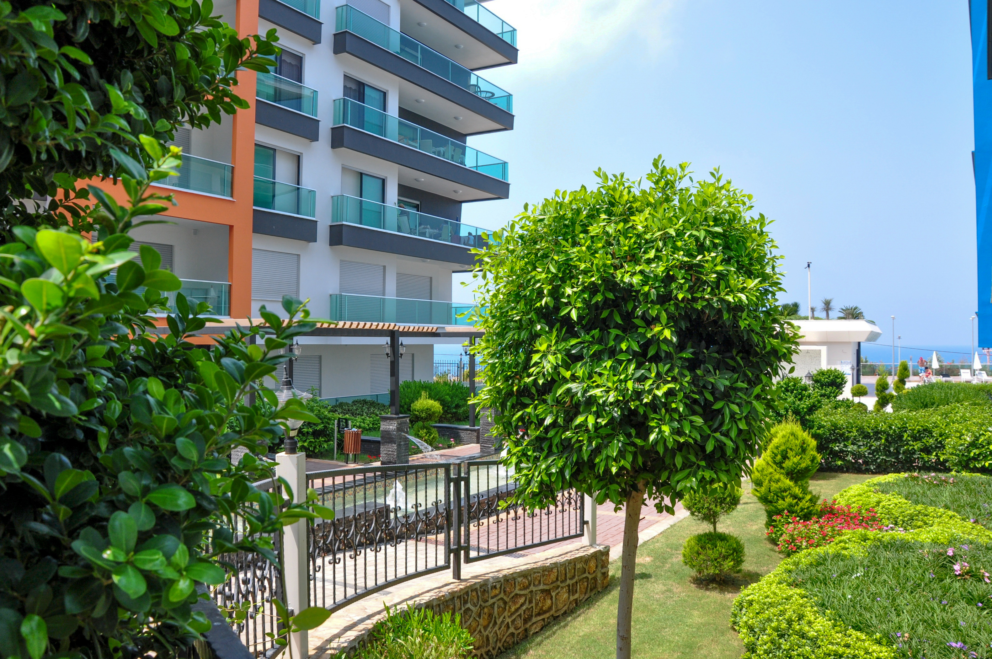 Well-kept garden with rounded shrubs and the sea visible between buildings in Kargicak, Turkey
