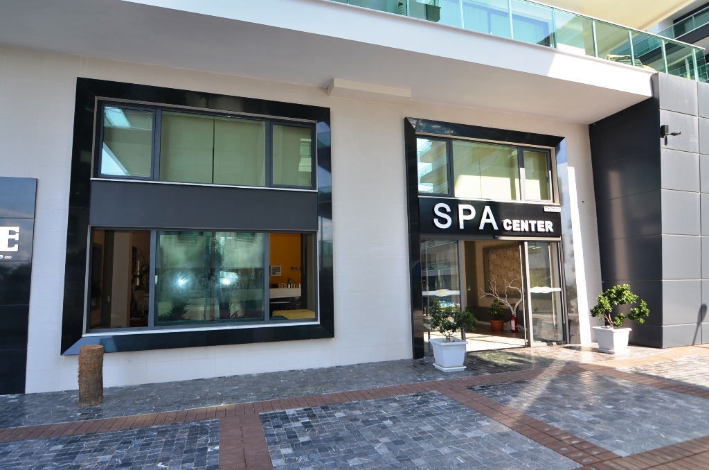 Spa entrance with a glass door and large facade windows beside a complex with apartments