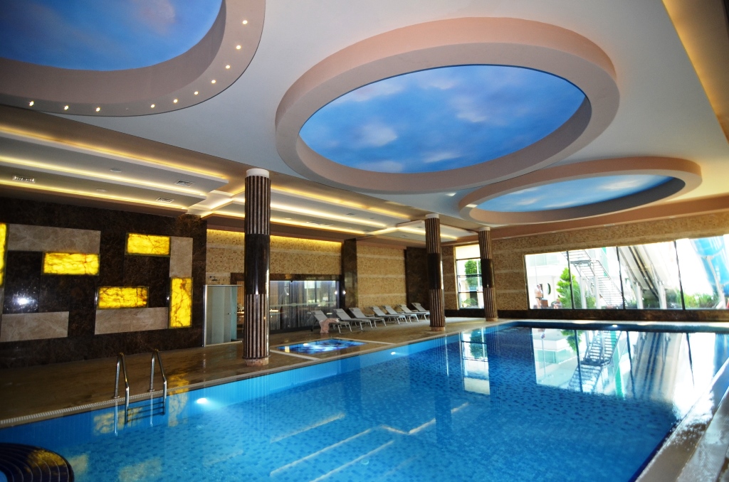 Indoor pool with blue mosaic, decorative columns and a whirlpool beside panoramic windows