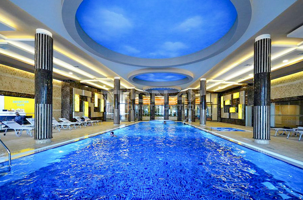 Long indoor pool with mosaic water and loungers in a complex with apartments for sale in Turkey